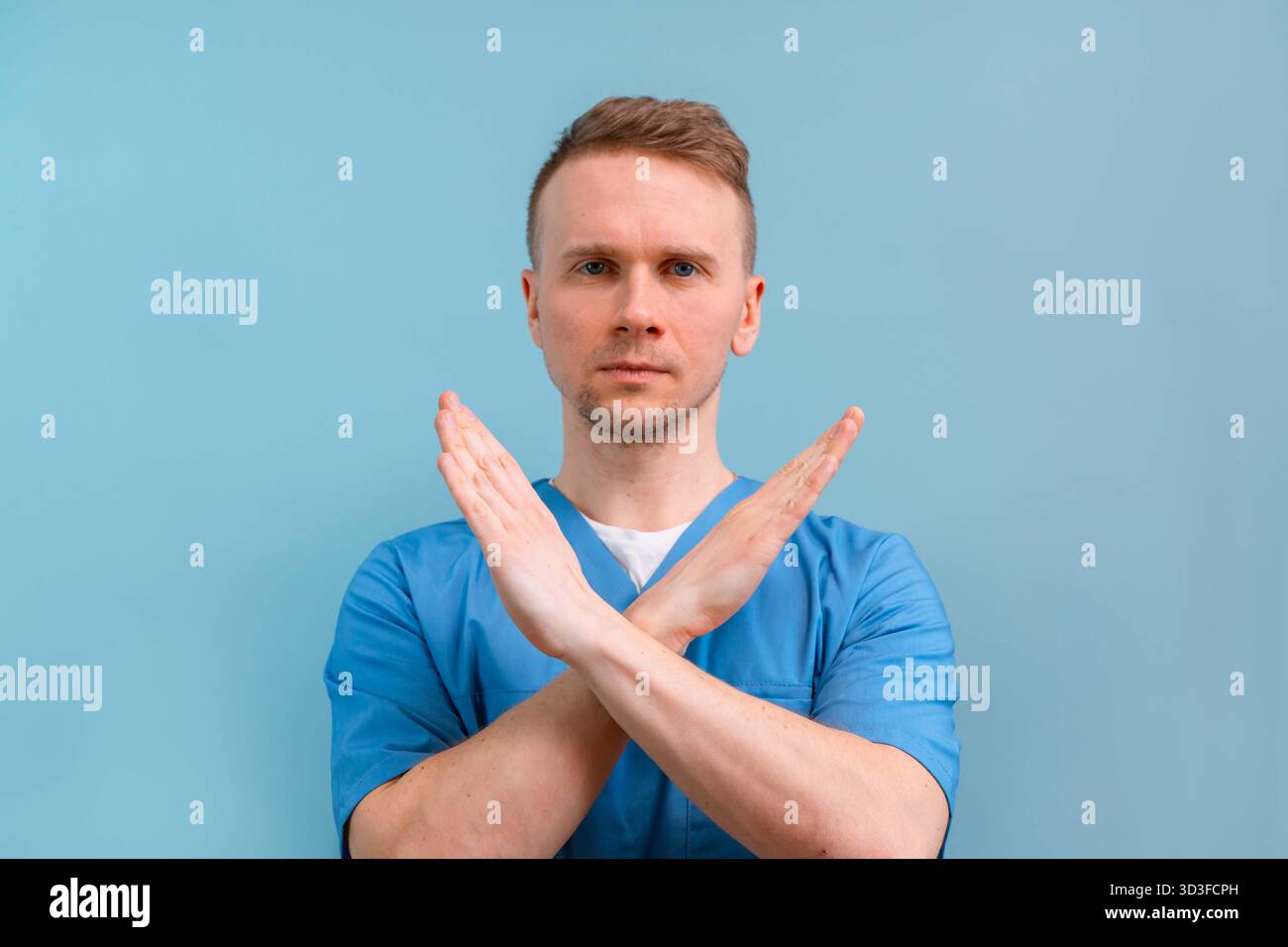 Un jeune médecin masculin dans un uniforme bleu hoche la tête négativement, interdit et conseille de ne pas le faire sur un fond isolé. geste de prohibitio Banque D'Images