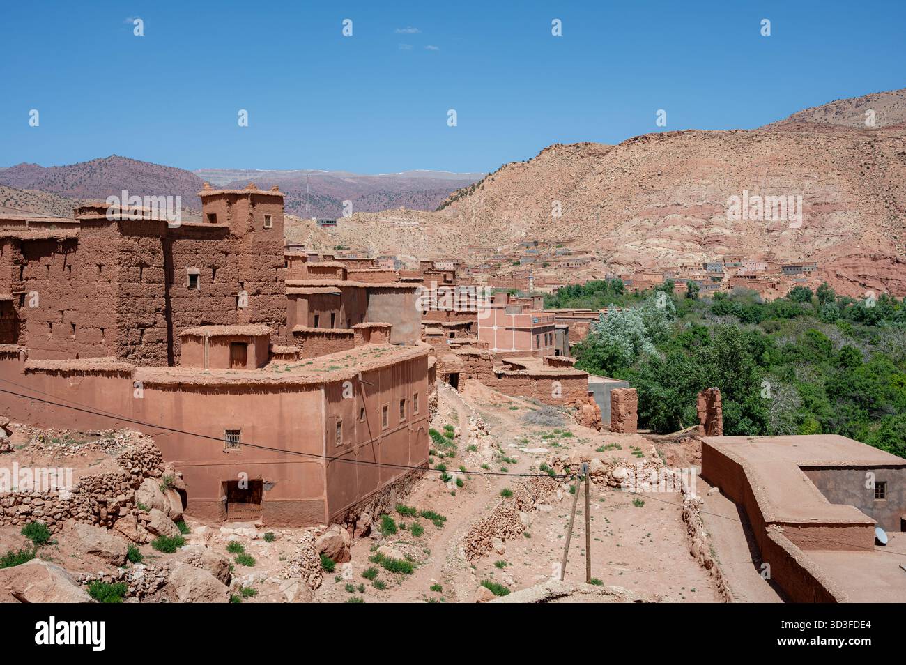 Bâtiments de boue rouge dans une oasis de palmiers contre des montagnes arides dans la vallée de l'Ounila, au Maroc, mettant en valeur l'architecture traditionnelle au milieu d'un paysage désertique Banque D'Images