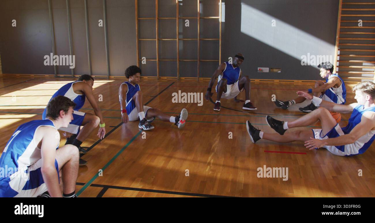 Des coéquipiers de basket-ball étirés portant des uniformes bleus et blancs sur le terrain de l'école, avec des barres d'escalade Banque D'Images