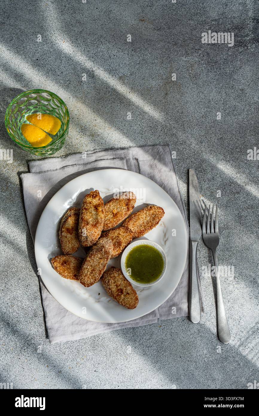 Filets de poulet frits croustillants servis sur une assiette blanche avec un côté de sauce aux prunes acieuses. Le plat est accompagné d'une boisson rafraîchissante au citron, créant un Banque D'Images