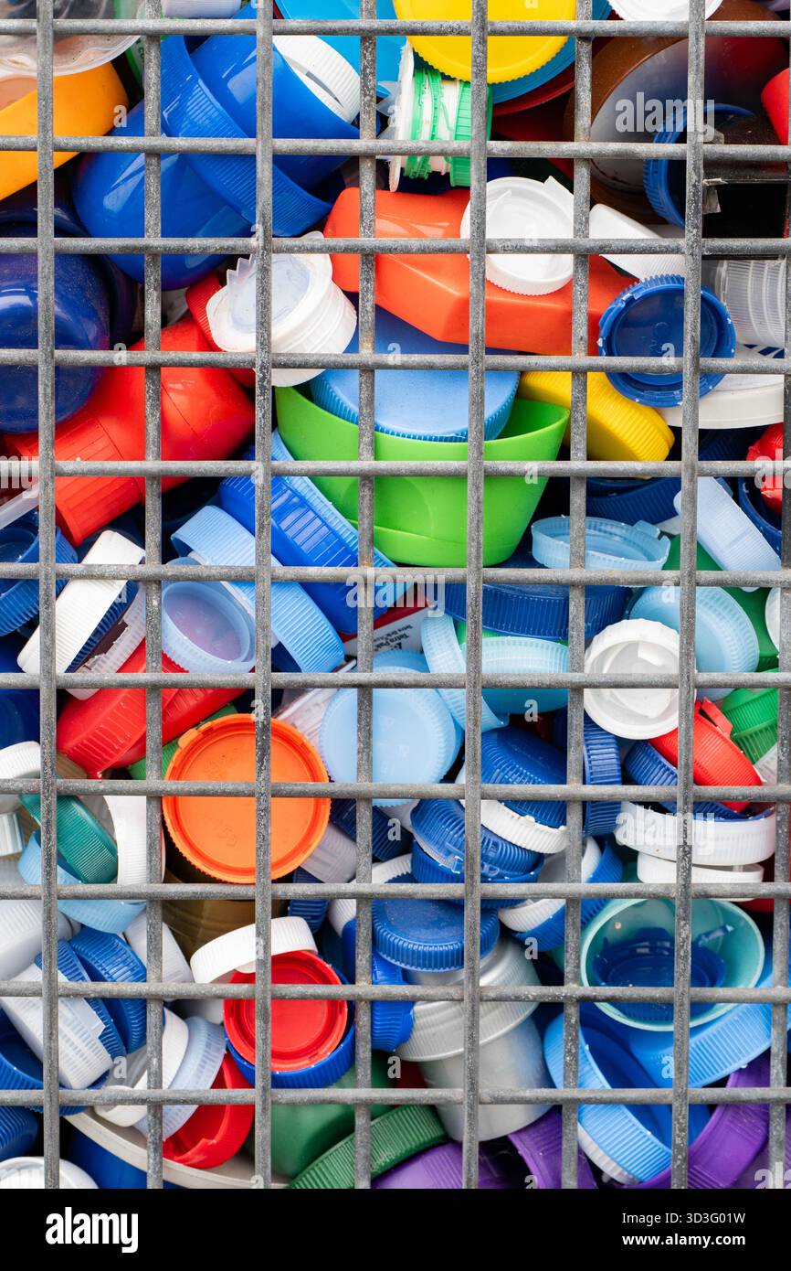 Une collection de bouchons de bouteilles en plastique colorés assortis est visible à travers les barres d'une cage de recyclage en métal. L'image souligne l'importance de Re Banque D'Images