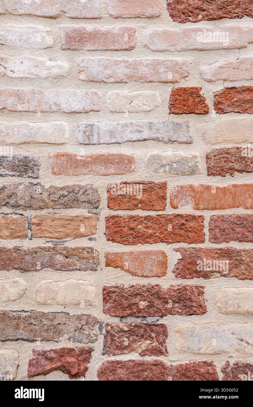 Vue rapprochée d'un mur de briques texturé avec un mélange de tons rouges et bruns. La surface vieillie affiche des nuances et des textures variables, créant un R Banque D'Images