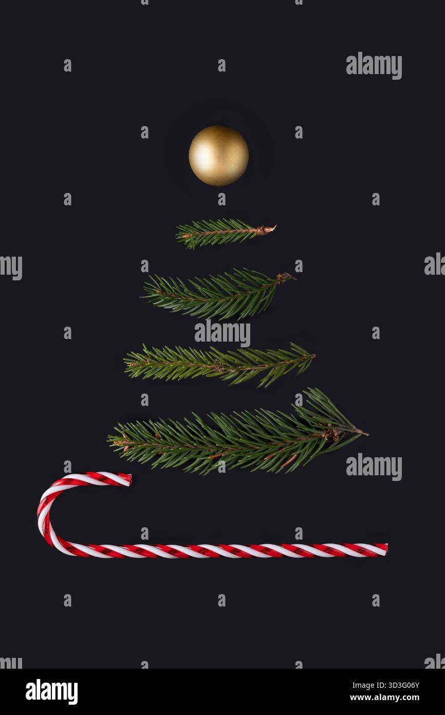 Arrangement artistique de bonbons et de branches de pin sur un fond noir, ressemblant à un arbre festif. La composition comprend une canne de bonbon et un doré Banque D'Images