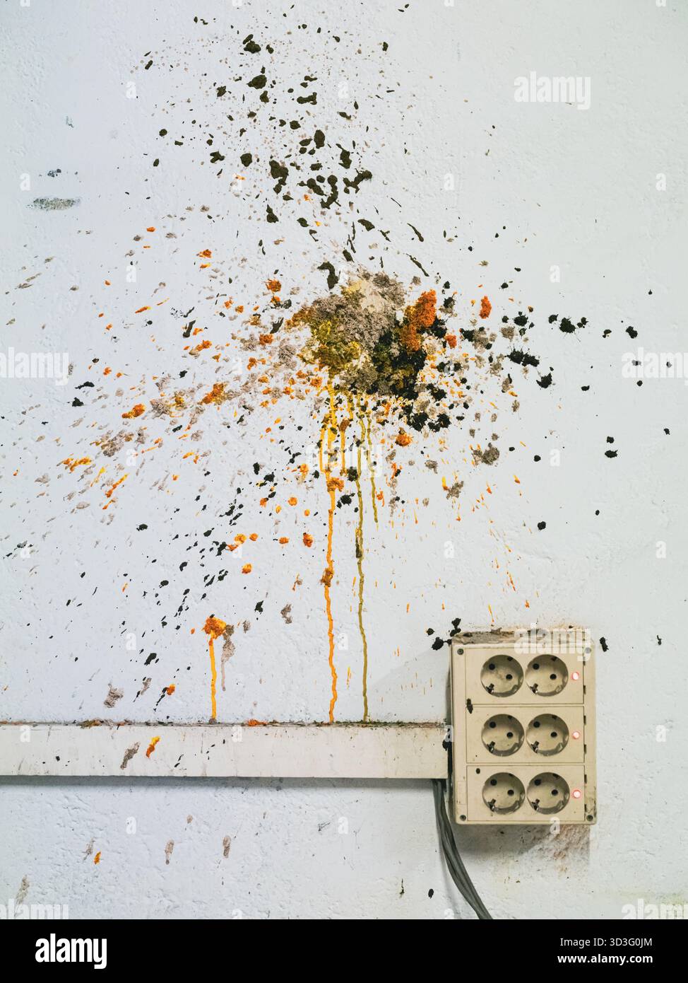 Une vieille prise électrique sur un mur usé, marquée par des éclaboussures de peinture colorées. L'image capture un mélange de négligence et d'expression artistique dans un aba Banque D'Images