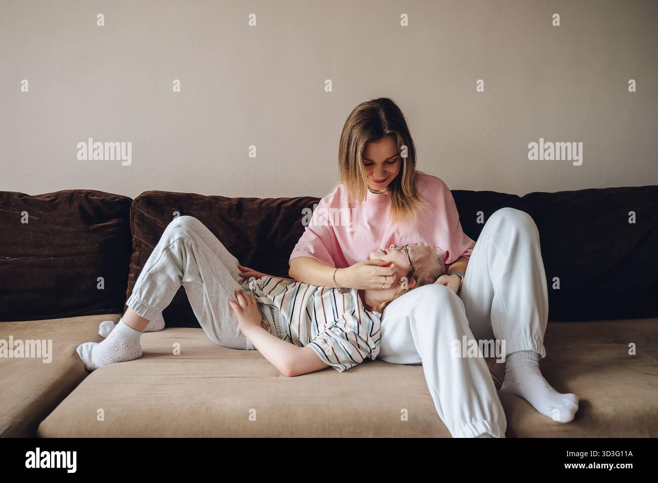Une mère aimante partage un moment tendre avec sa fille atteinte du syndrome de Down. Ils sont assis confortablement sur le canapé, appréciant la compagnie de l'autre Banque D'Images