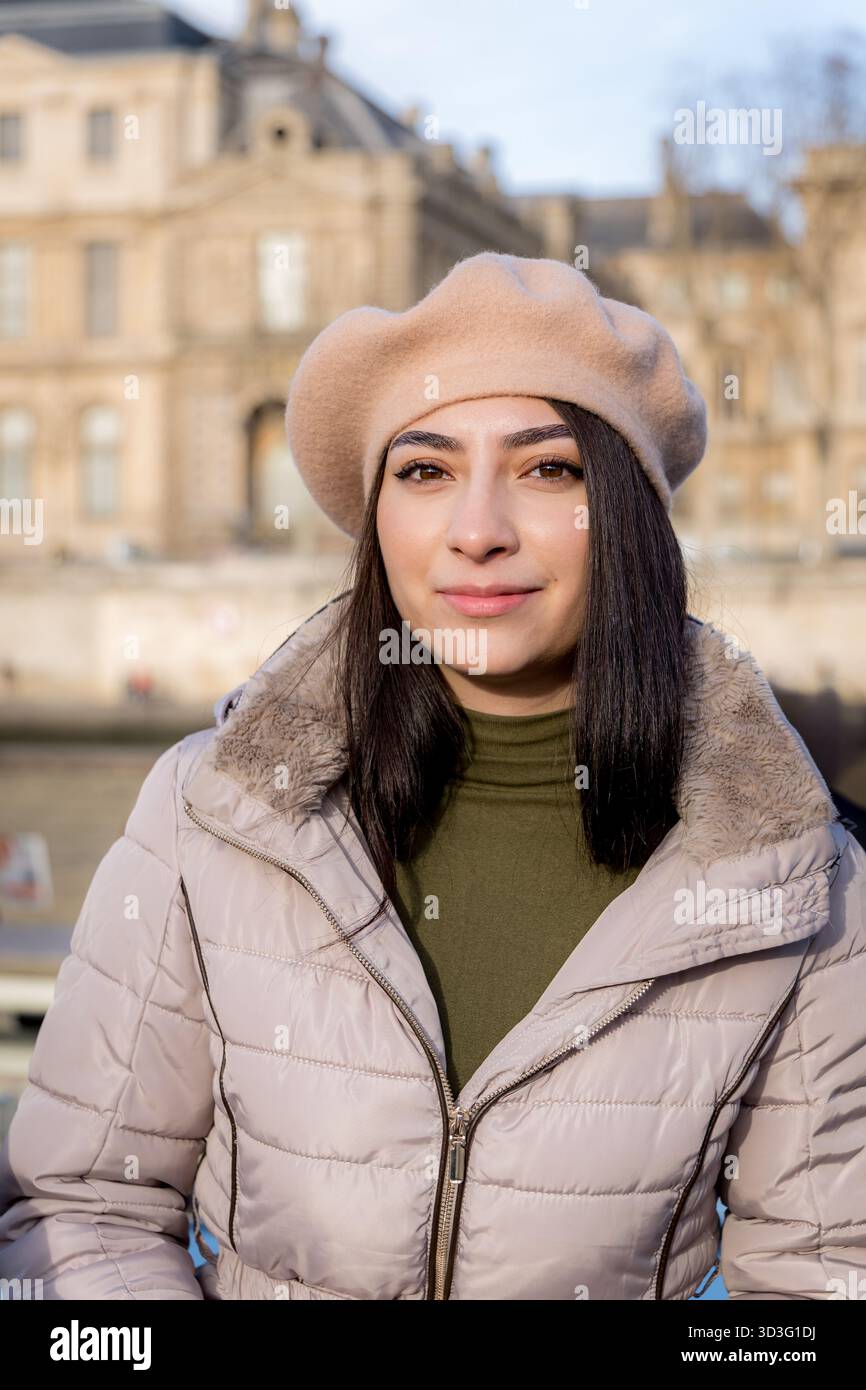 Une femme est capturée à Paris portant un béret beige et une veste d'hiver. Sa tenue élégante complète l'architecture parisienne classique dans le backgr Banque D'Images