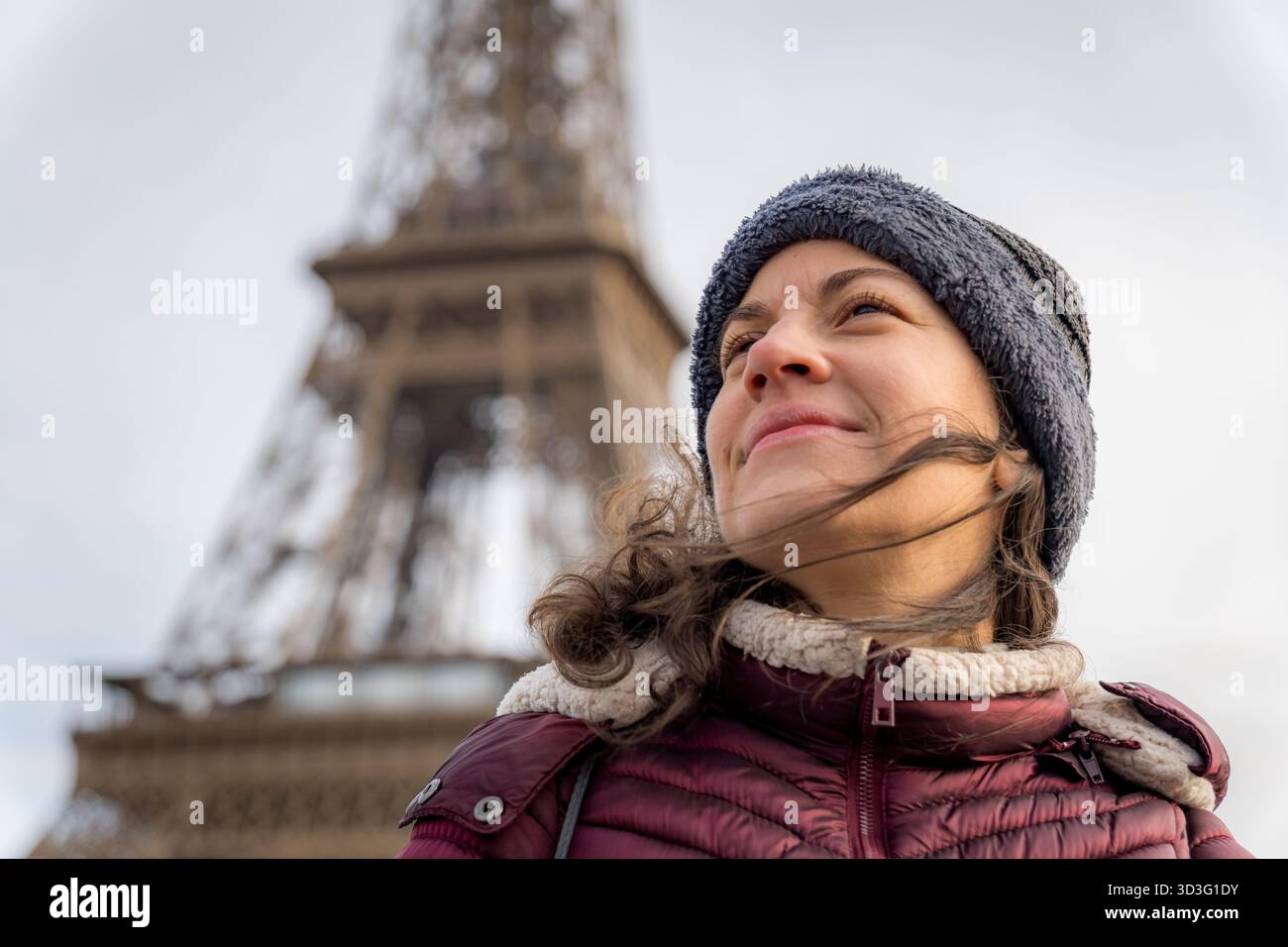 Une femme profite d'une journée fraîche à Paris, debout en toute confiance devant l'emblématique Tour Eiffel. Son expression reflète la joie et le contentement, capturant Banque D'Images