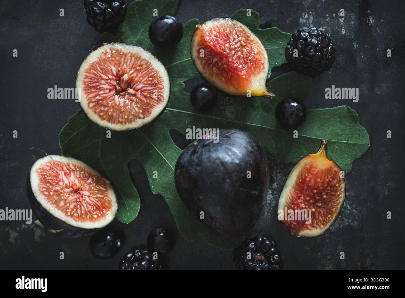 Figues noires fraîches, bleuets et mûres magnifiquement disposées sur des feuilles vertes avec un fond sombre Banque D'Images
