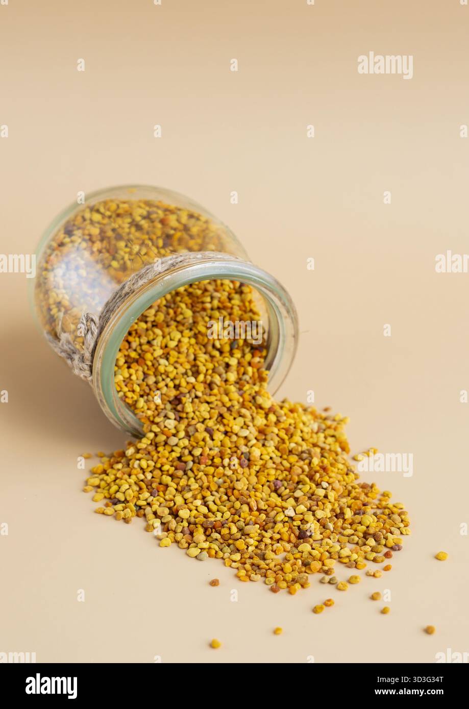Un bocal en verre renverse du pollen d'abeille naturel éclatant sur un fond beige lisse. Ce superaliment est riche en vitamines, minéraux et enzymes, idéal pour le holo Banque D'Images