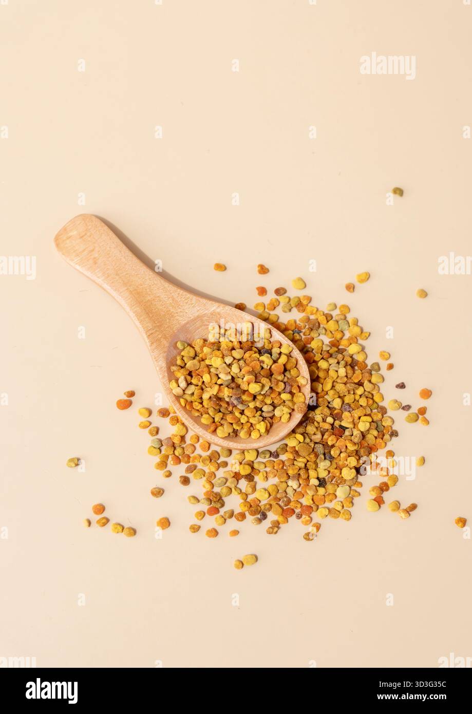 Vue de dessus de granules de pollen d'abeille dispersés sur une surface de couleur crème avec une cuillère en bois. Les couleurs vives du pollen contrastent avec le dos doux Banque D'Images