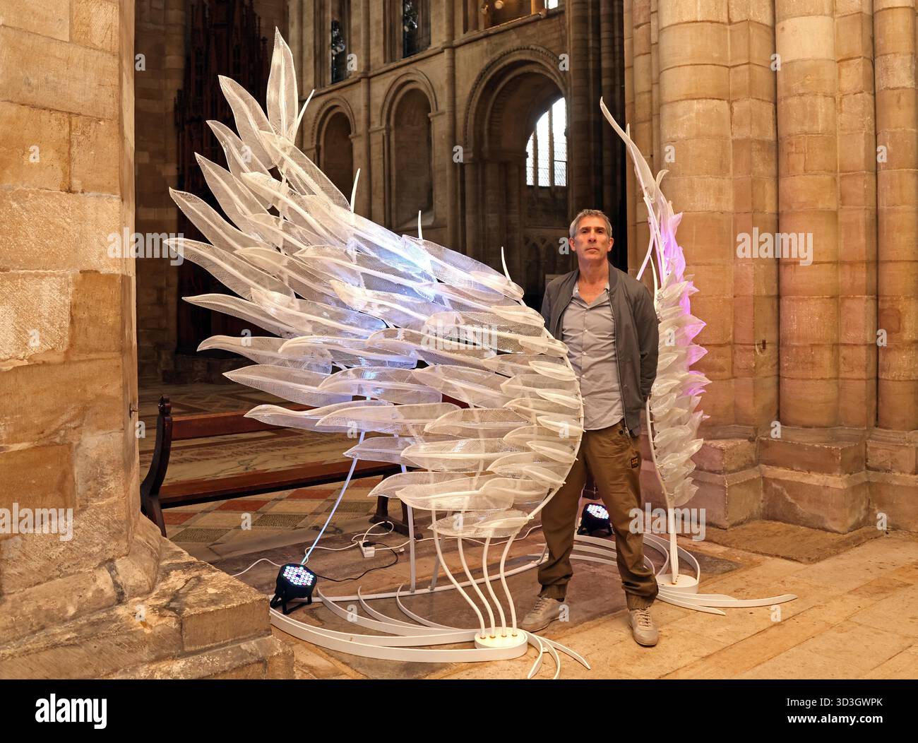 Une sculpture frappante en forme d'aile de verre, « Solace », a été exposée à la cathédrale de Peterborough. Créé par l'artiste Layne Rowe (photo), et debout à 10 pieds de haut, Solace est une paire d'ailes de verre chatoyantes, symbolisant la liberté, la fragilité, la force et la protection. Créée à partir de plus de 100 plumes de verre sculptées individuellement à chaud, chaque plume présente une fine toile blanche pour évoquer la nature légère et fluide des ailes réelles. Le cadre en fer et l'éclairage subtil donnent vie à la pièce, projetant une lueur éthérée. Sculpture d'aile de verre 'Solace' à la cathédrale de Peterborough, Peterborough, Cambridgeshire, Banque D'Images