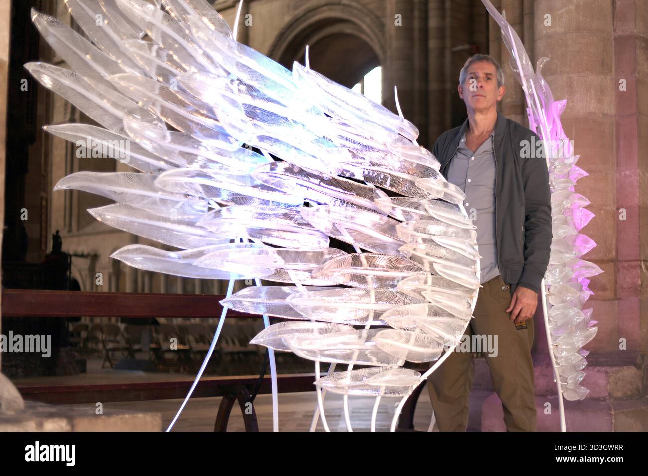 Une sculpture frappante en forme d'aile de verre, « Solace », a été exposée à la cathédrale de Peterborough. Créé par l'artiste Layne Rowe (photo), et debout à 10 pieds de haut, Solace est une paire d'ailes de verre chatoyantes, symbolisant la liberté, la fragilité, la force et la protection. Créée à partir de plus de 100 plumes de verre sculptées individuellement à chaud, chaque plume présente une fine toile blanche pour évoquer la nature légère et fluide des ailes réelles. Le cadre en fer et l'éclairage subtil donnent vie à la pièce, projetant une lueur éthérée. Sculpture d'aile de verre 'Solace' à la cathédrale de Peterborough, Peterborough, Cambridgeshire, Banque D'Images