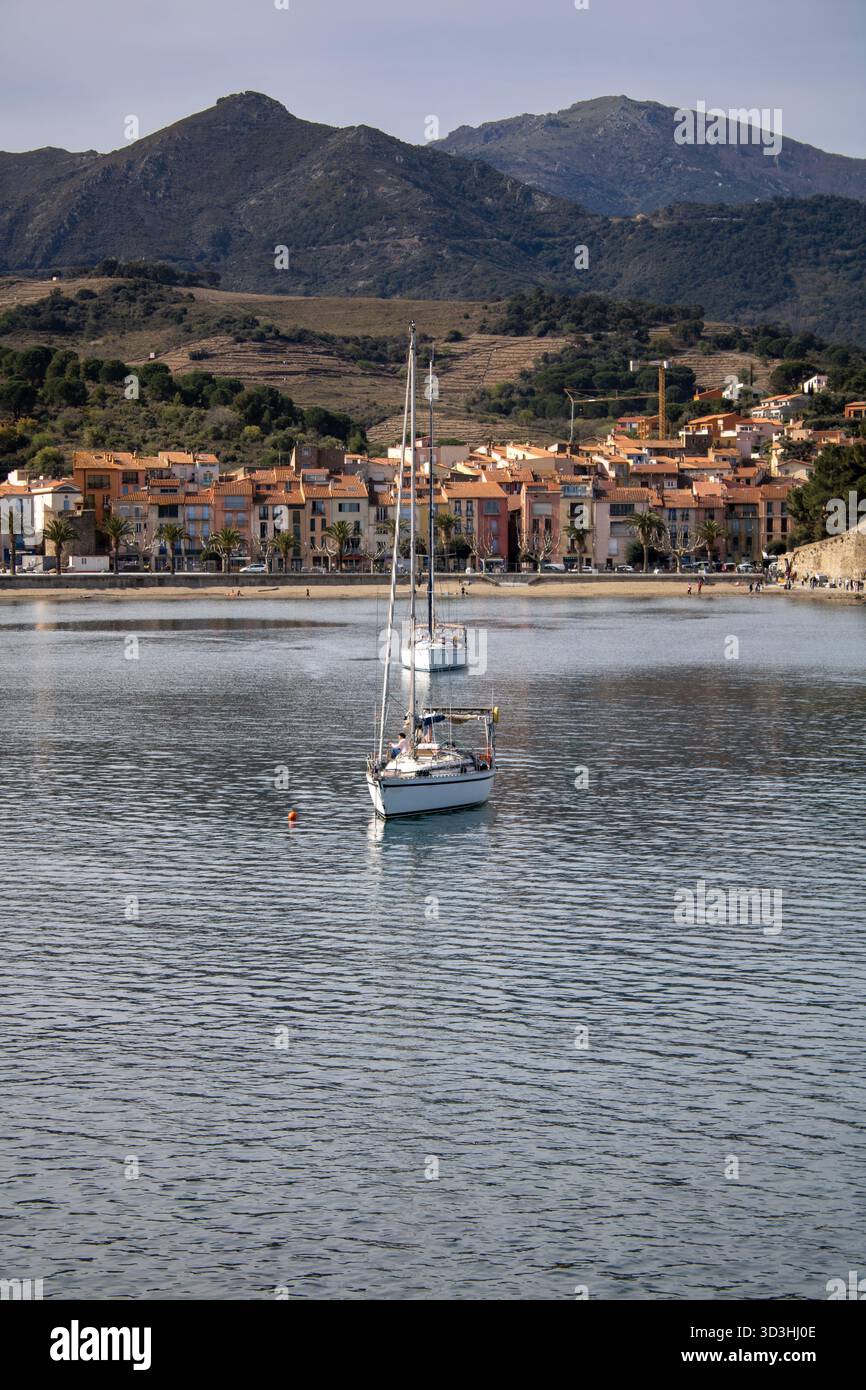 Village de Collioure présentant une architecture traditionnelle et des voiliers ancrés dans la baie tranquille, avec des montagnes formant une toile de fond pittoresque Banque D'Images