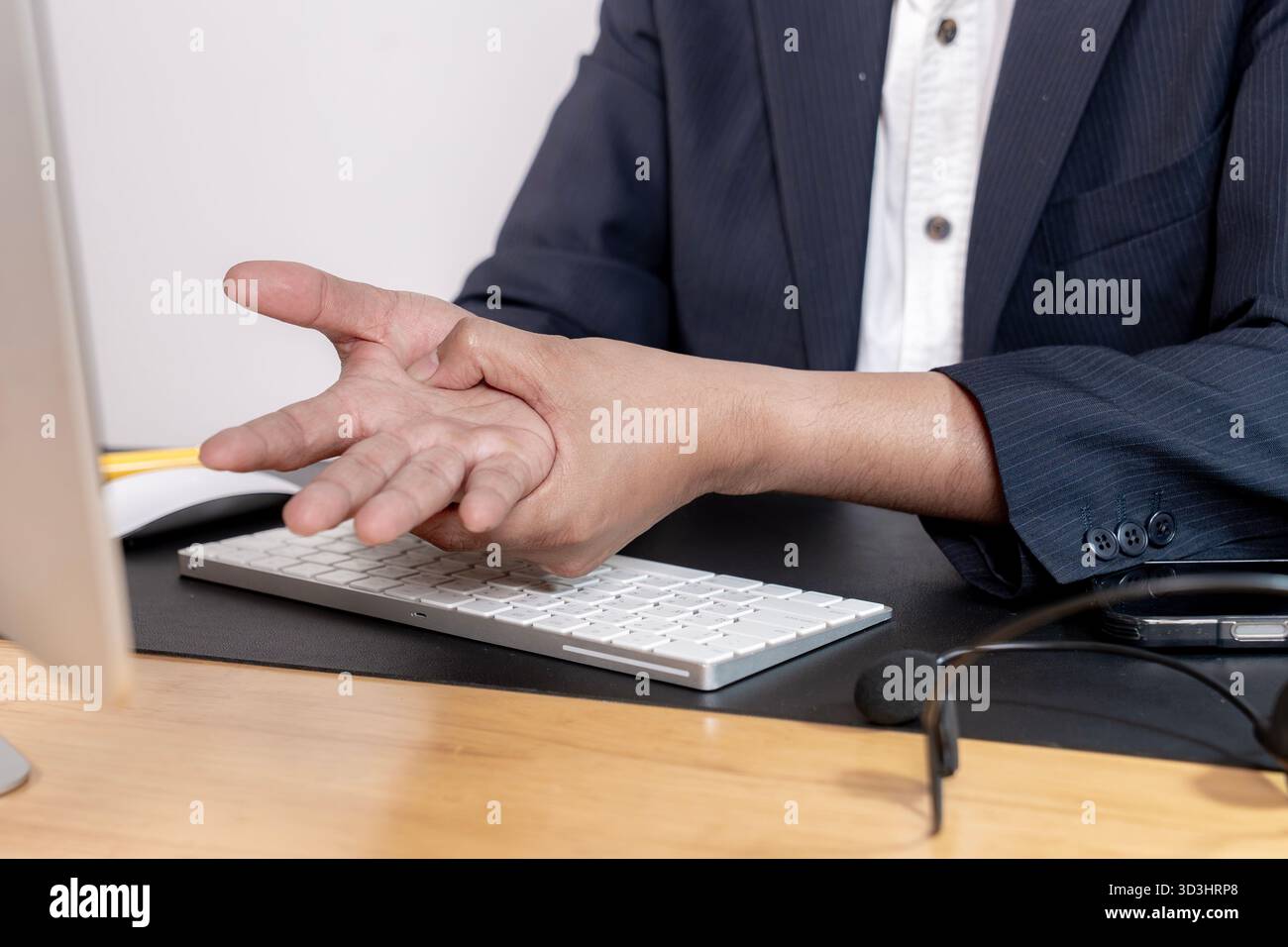 Employé de bureau tenant le poignet dans la douleur tout en utilisant un ordinateur, symbolisant le syndrome de bureau et les préoccupations de santé. Banque D'Images