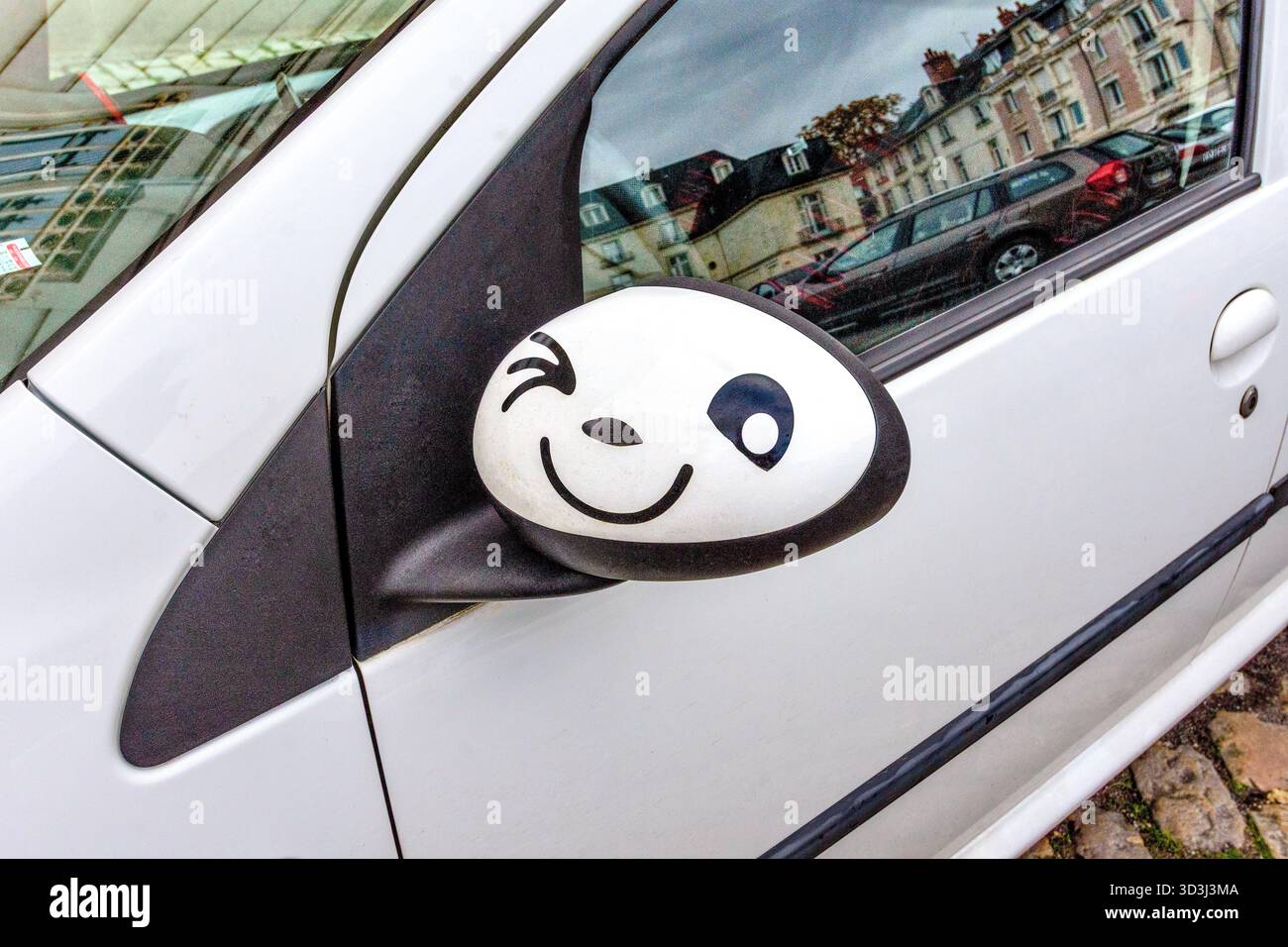 Illustration drôle de visage claquant peinte à la main sur le rétroviseur extérieur d'une Citroën C1 - Tours, Indre-et-Loire (37), France. Banque D'Images
