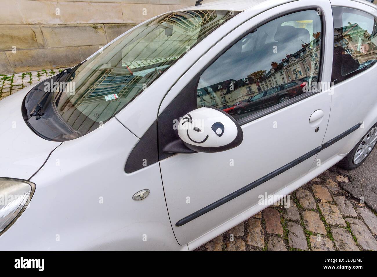 Illustration drôle de visage claquant peinte à la main sur le rétroviseur extérieur d'une Citroën C1 - Tours, Indre-et-Loire (37), France. Banque D'Images