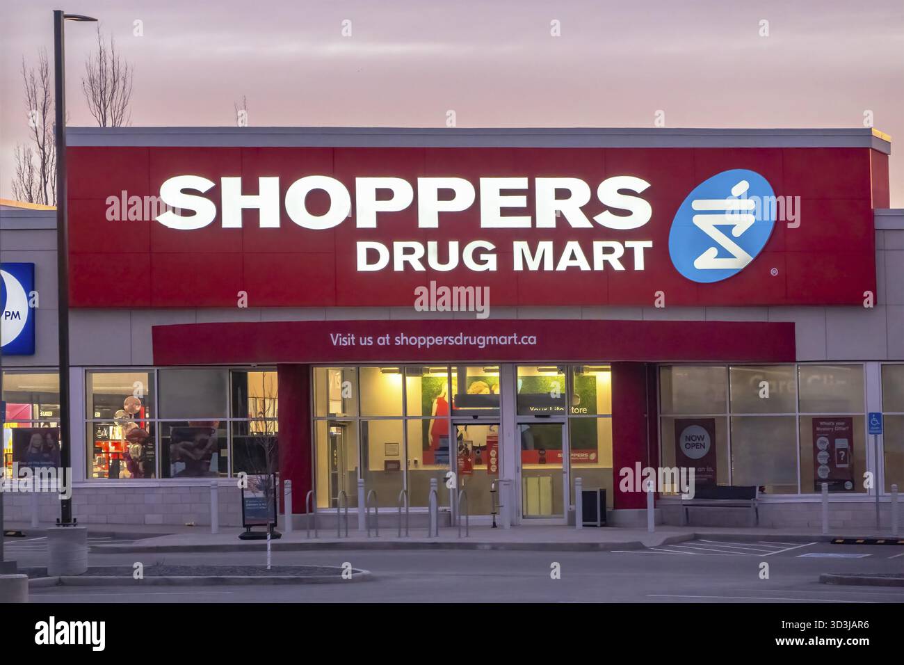 Calgary, Alberta, Canada. 23 mars 2025. Un magasin Shoppers Drug Mart au crépuscule, avec une vitrine illuminée en rouge et blanc avec le lo de la société Banque D'Images