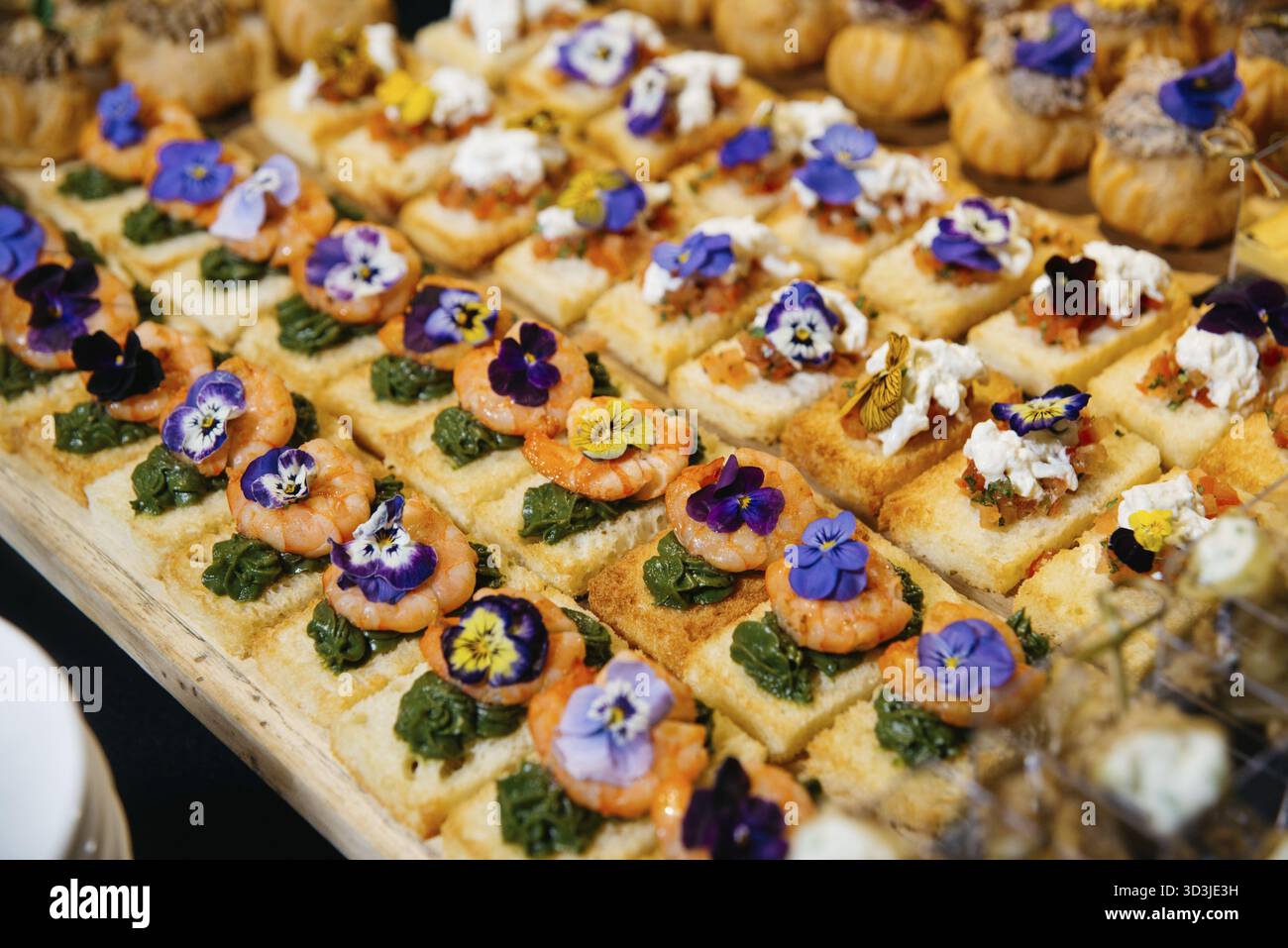 Nourriture, canapés élégants en bouchée garni de crevettes, pesto, mélange bruschetta et fleurs comestibles, servis sur du pain grillé pour les événements de restauration Banque D'Images