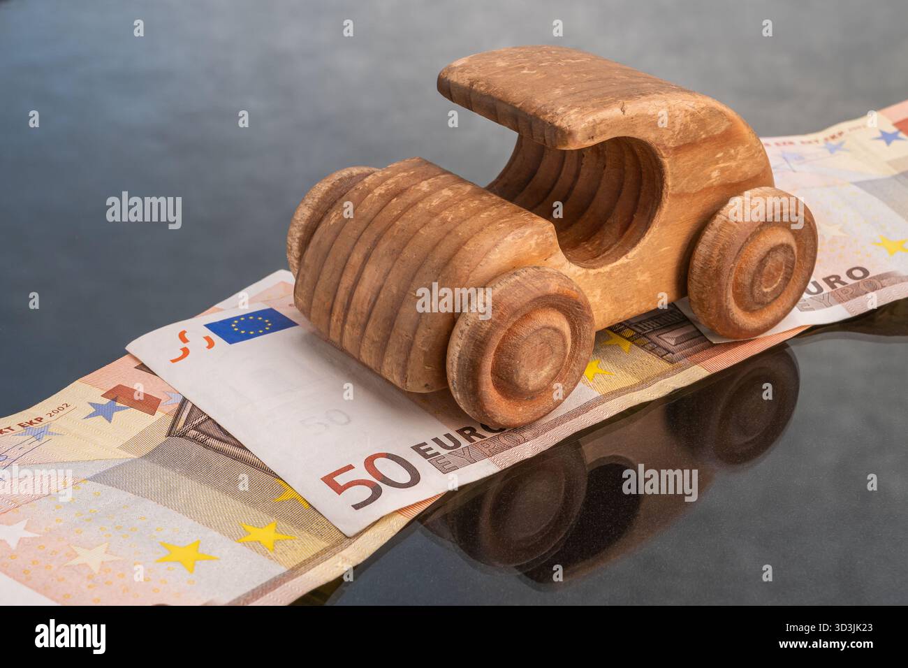 La voiture jouet en bois se déplace sur une pile de billets de 50 euros, représentant les coûts de transport et le financement. Banque D'Images