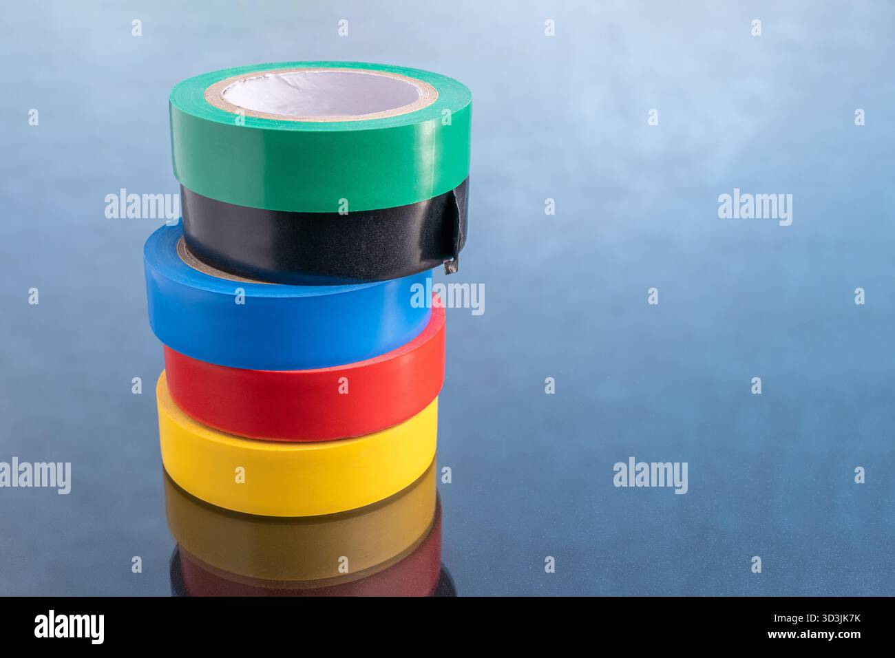 Rouleaux de ruban électrique coloré empilés verticalement sur une surface sombre et réfléchissante, représentant la sécurité, la réparation ou l'organisation Banque D'Images