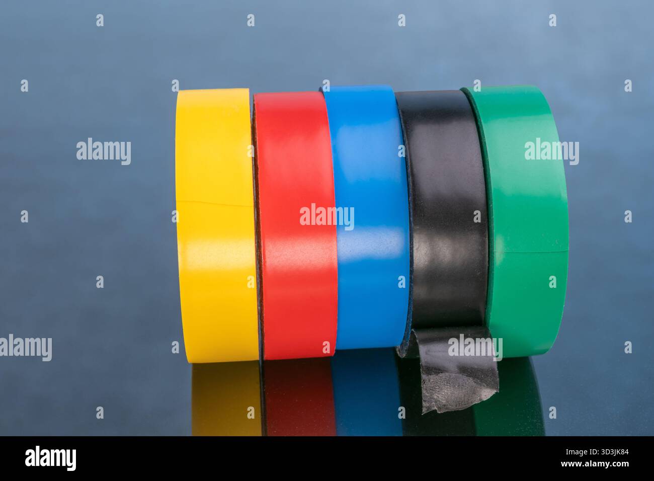 Cinq rouleaux de ruban électrique coloré pour les réparations, sur une surface réfléchissante. Banque D'Images