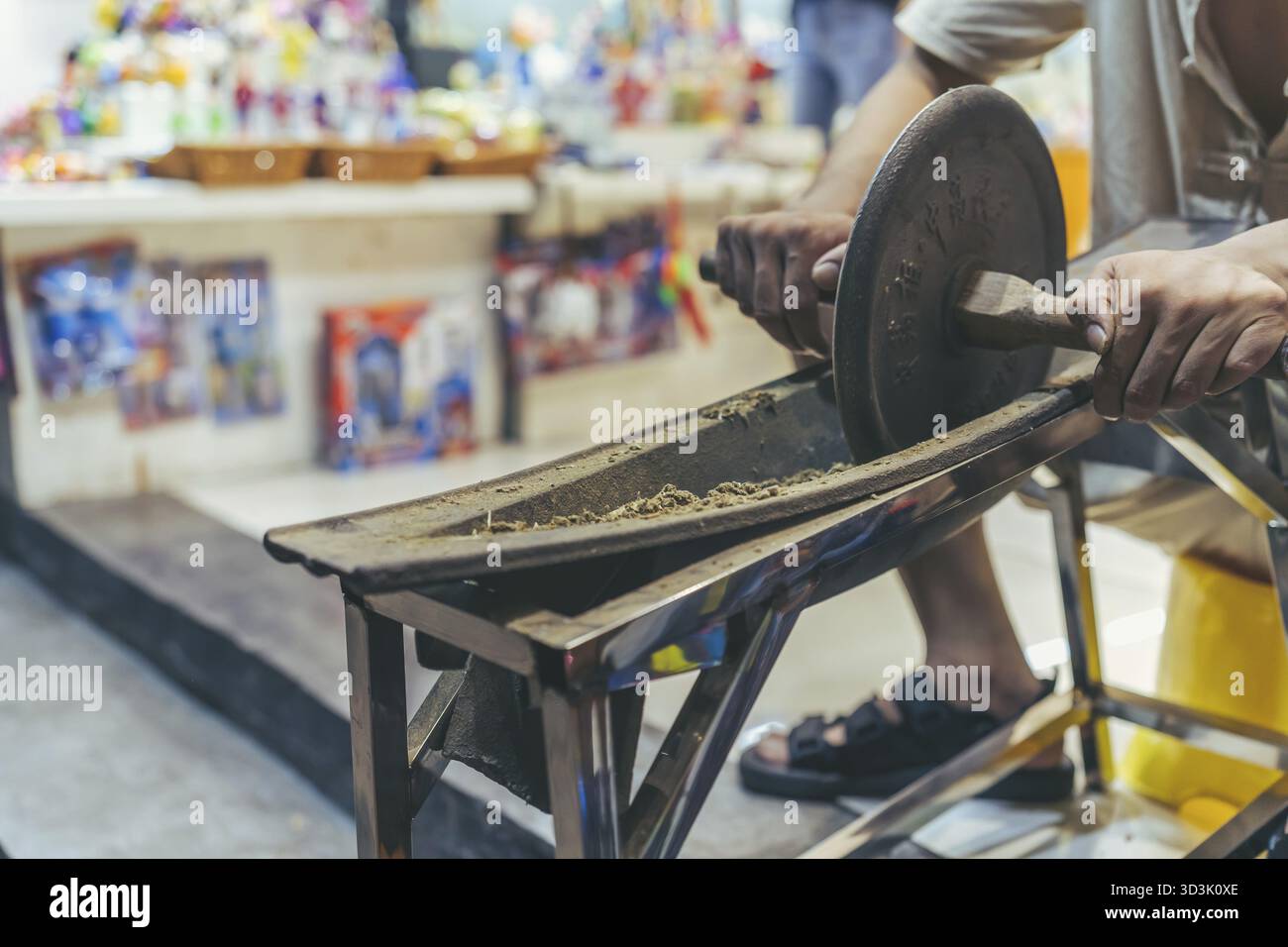 Feng Huang, Chine - août 2019 : homme roulant un outil rond lourd avec des poignées et écrasant la matière organique à l'intérieur d'une forme dans un petit atelier de souvenirs Banque D'Images