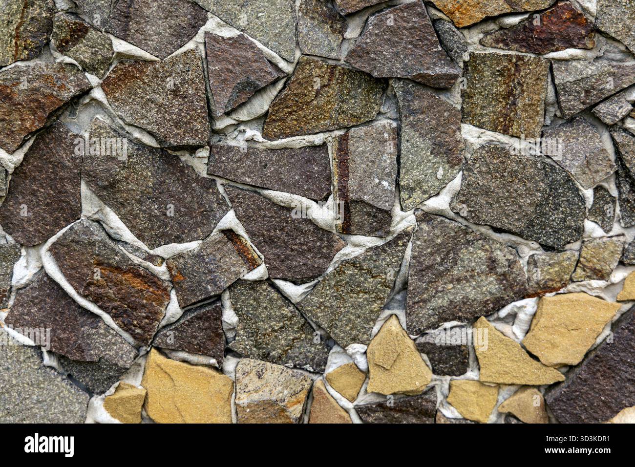 Fond irrégulier de texture de mur de pierre. Gros plan d'un mur décoratif fait de morceaux de pierre naturelle inégaux dans des tons terreux, créant un et rugueux Banque D'Images