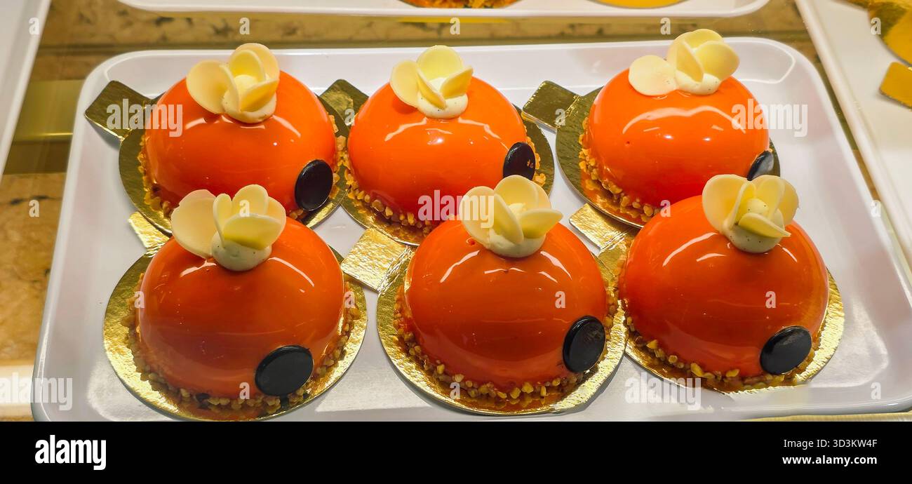 Les desserts glacés à l'orange sont magnifiquement disposés sur un plateau blanc, avec des décorations florales délicates et une finition brillante, mettant en valeur l'artiste culinaire - Image de stock capturée avec un smartphone