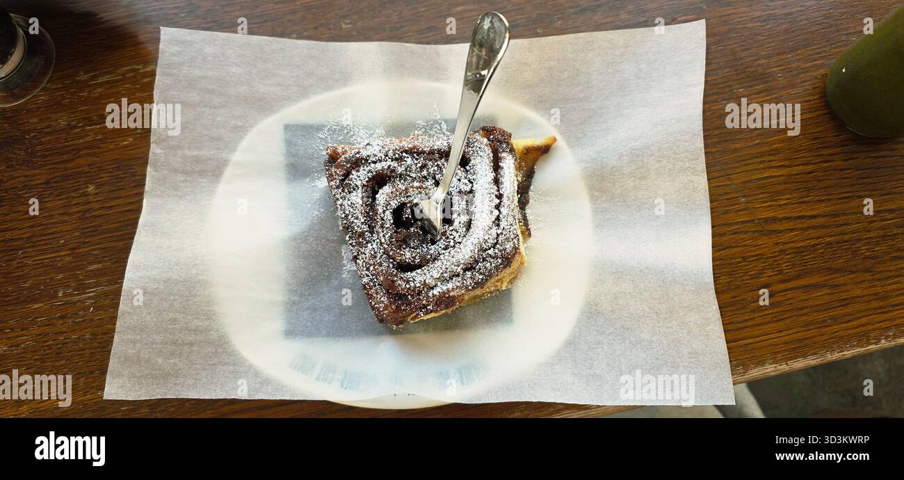 Une délicieuse pâtisserie au chocolat garnie de sucre en poudre, posée sur du papier parchemin, reposant sur une table en bois rustique, invitante et appétissante. - Image de stock capturée avec un smartphone