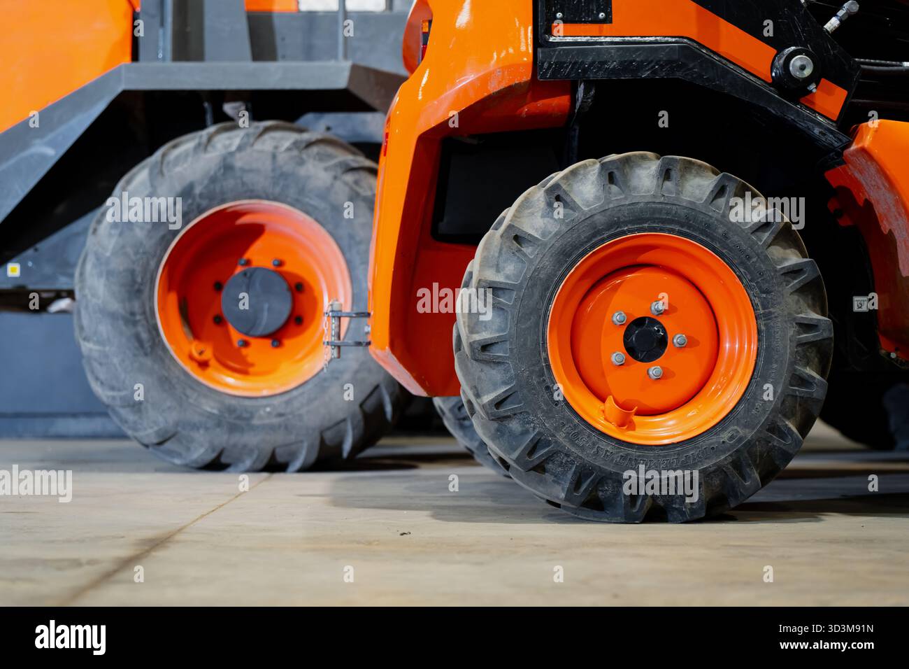 Gros plan de pneus de véhicules de construction avec jantes en acier orange sur sol en béton montrant un motif de bande de roulement profond, une texture en caoutchouc et une conception industrielle Banque D'Images