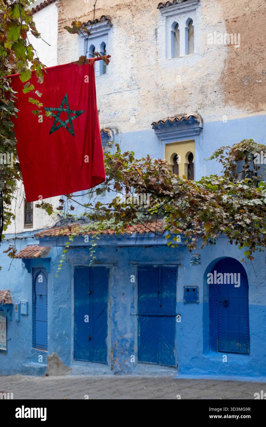 Une rue pittoresque de Chefchaouen, avec ses façades bleues, ornée d'un drapeau marocain. Banque D'Images