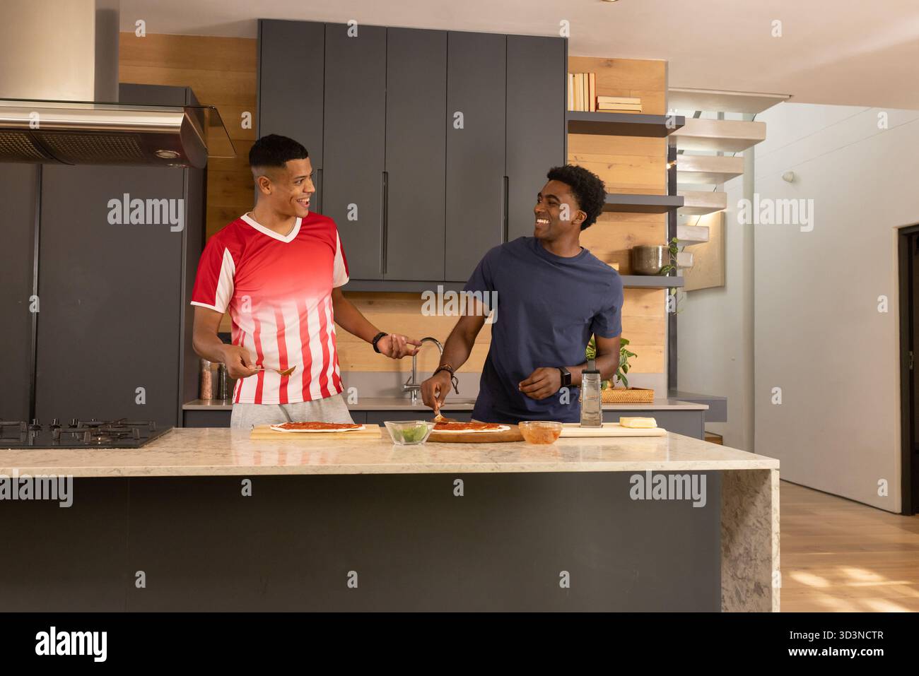 Saupoudrer de fromage, divers amis masculins préparant des bases de pizza sur l'île de marbre avec de la sauce, des herbes Banque D'Images