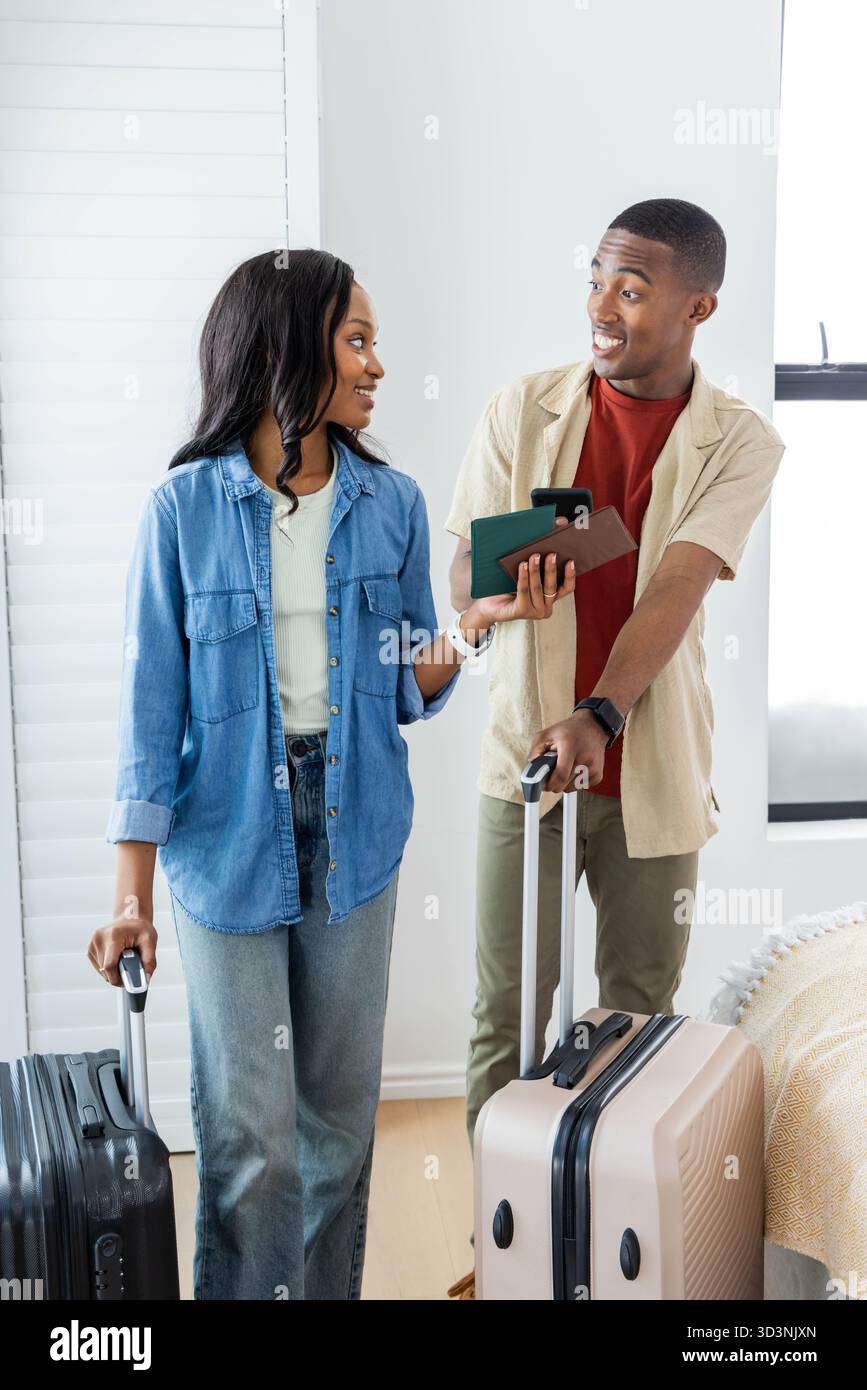 Tirant des valises et tenant des passeports afro-américains couple dans une chambre lumineuse Banque D'Images