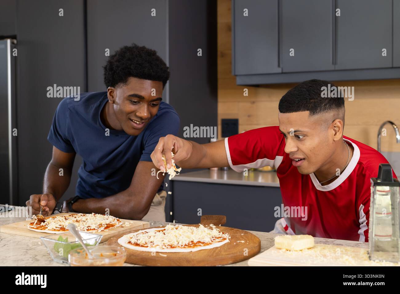 Souriant divers amis masculins faisant des pizzas maison à l'îlot de cuisine, avec des planches à pizza et du fromage Banque D'Images