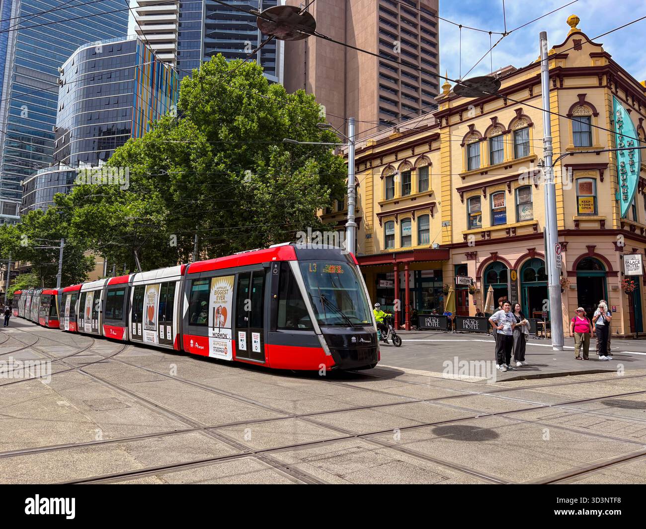Tramway de Sydney Light Rail voyageant le long d'une rue de la ville, avec une architecture historique comme le Palace Hotel et des gratte-ciel modernes en arrière-plan. Banque D'Images