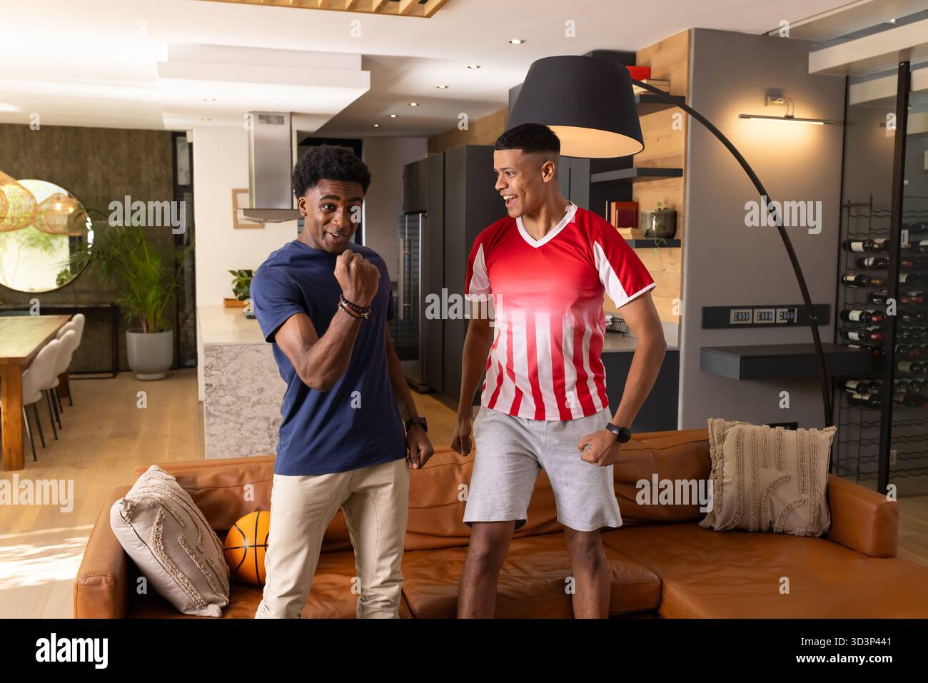 Acclamer divers amis masculins debout dans le salon ouvert, avec basket-ball sur le canapé Banque D'Images