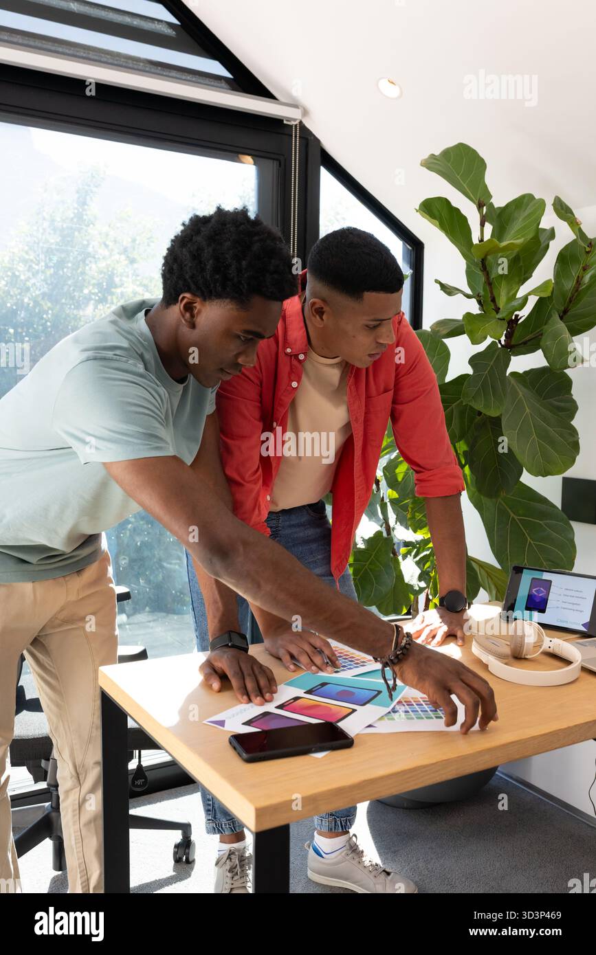 Penchant divers collègues masculins examinant des échantillons à la table du studio sous la lucarne, avec tablette Banque D'Images
