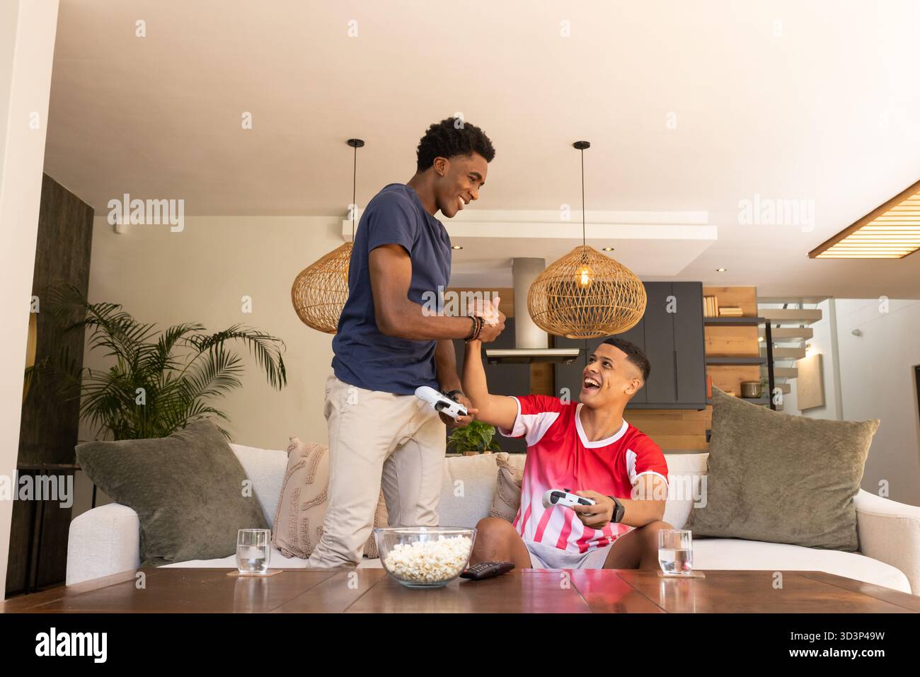 Célébrer divers amis masculins échangeant la bosse du poing dans le salon, avec pop-corn et contrôleurs Banque D'Images