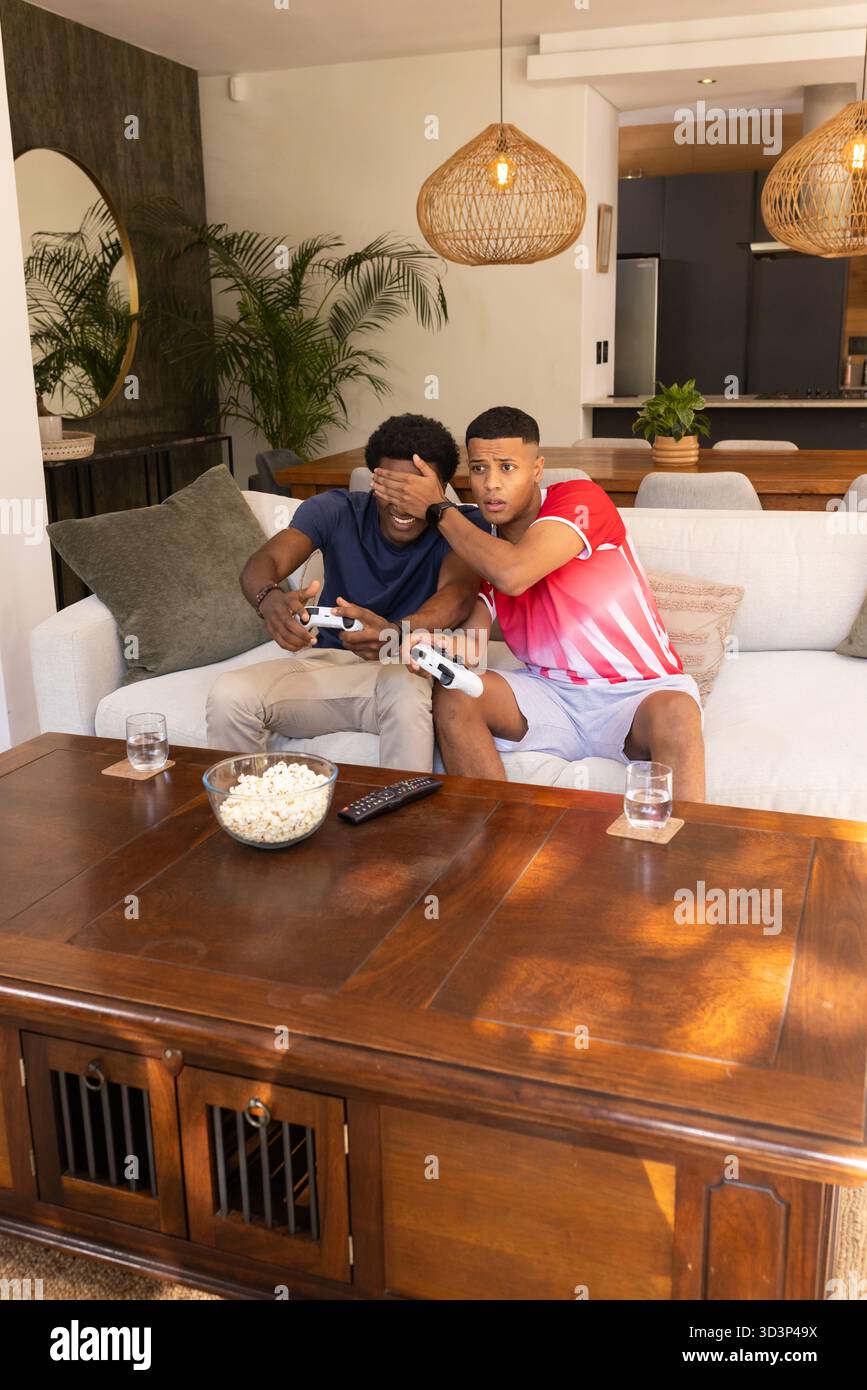 Jouer divers amis masculins assis sur un canapé léger dans le salon, avec des contrôleurs et pop-corn Banque D'Images