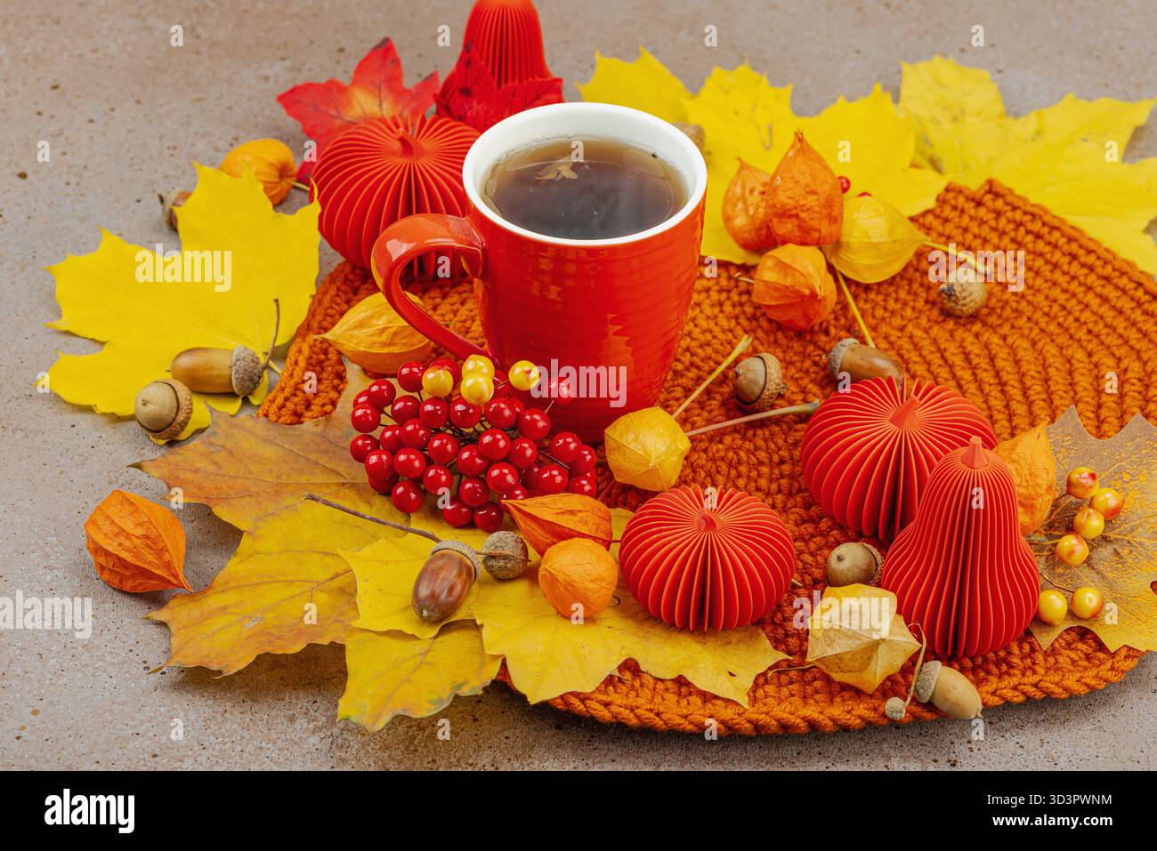 Nature morte d'automne avec une tasse de thé rouge, des baies de viburnum, des glands, des feuilles d'érable jaunes et un décor artisanal dans des tons chaleureux et confortables, symbolisant la vie lente Banque D'Images
