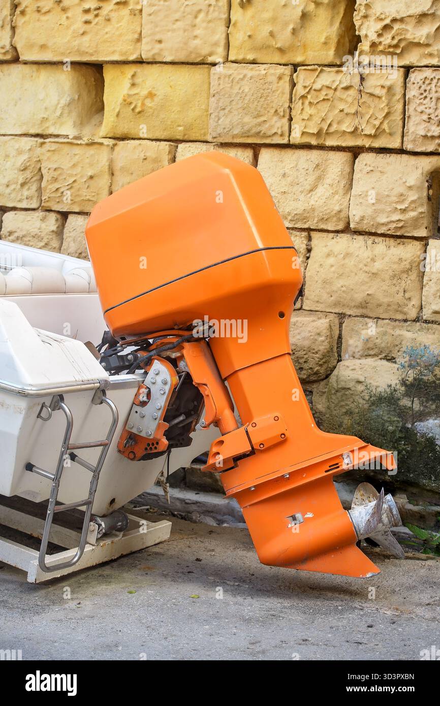 Gros plan d'un moteur hors-bord marin orange vif monté sur un petit bateau blanc à côté d'un mur de pierre. Banque D'Images