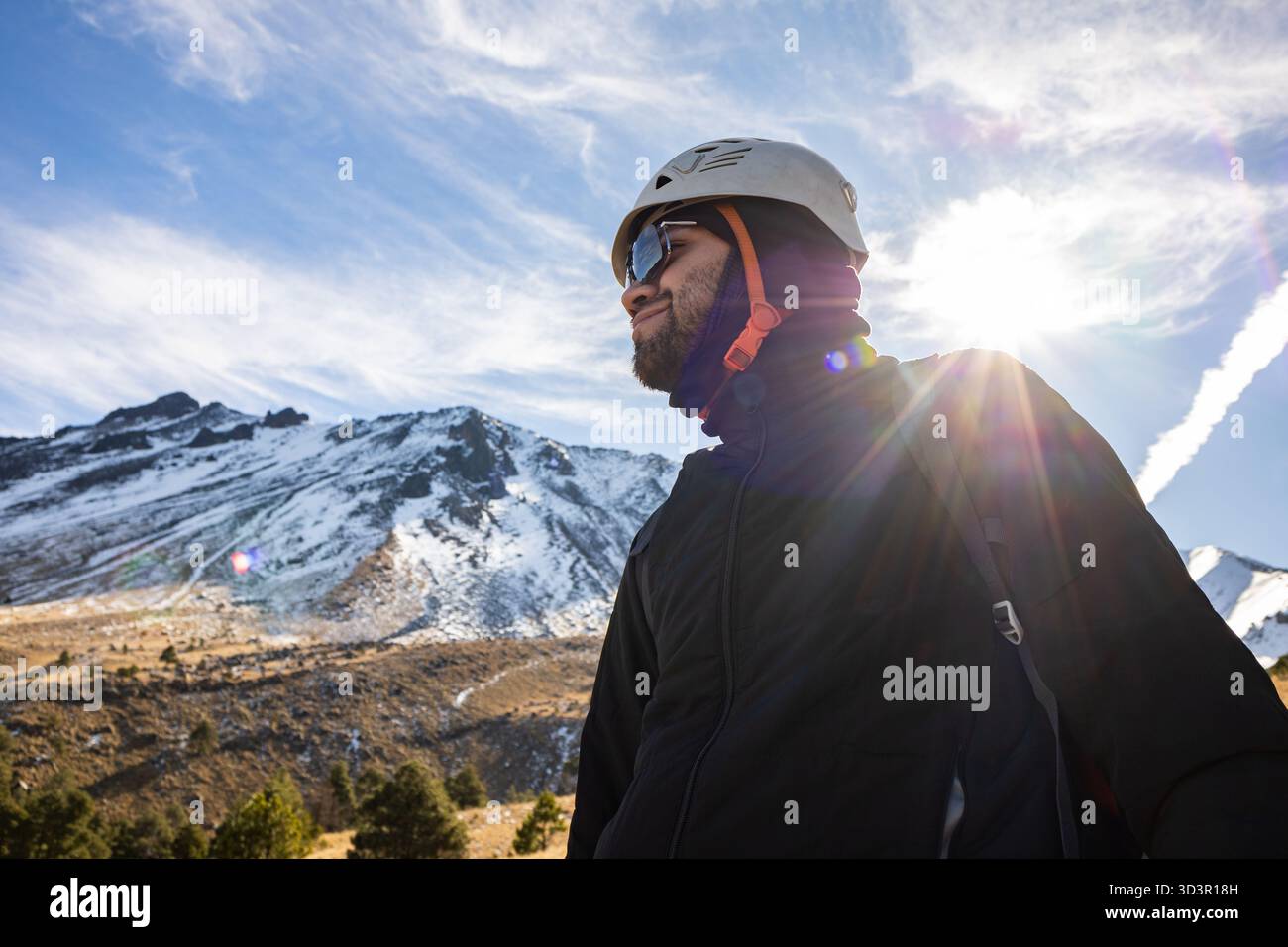 Un randonneur se tient en confiance dans l'équipement d'hiver, avec des montagnes glacées et un ciel lumineux en arrière-plan, mettant en valeur le frisson de la randonnée hivernale et alpine ex Banque D'Images