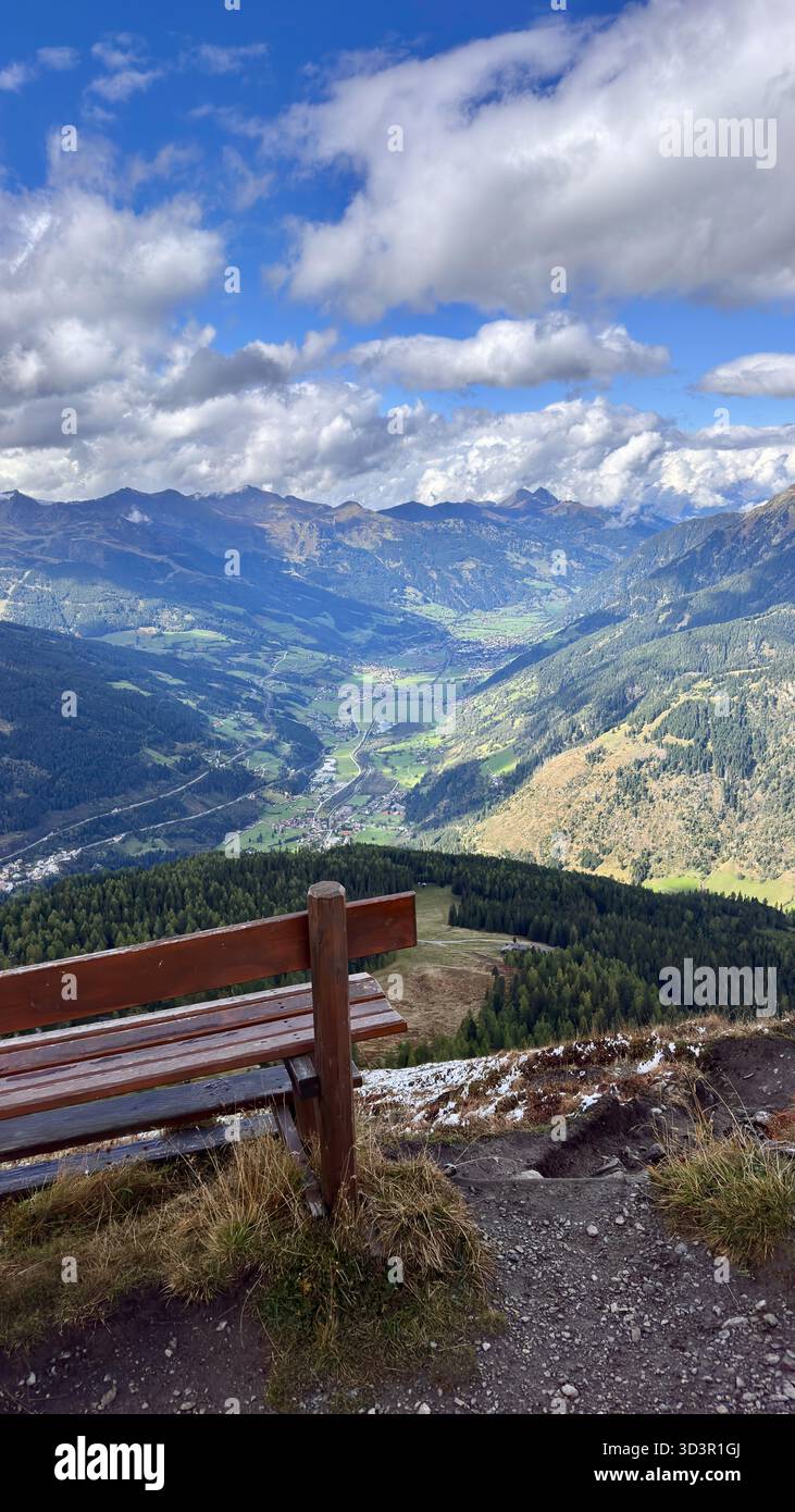 Un banc en bois rustique surplombe la magnifique vallée de Gastein dans les Alpes autrichiennes, avec des forêts verdoyantes et des sommets montagneux lointains sous une fille du ciel Banque D'Images