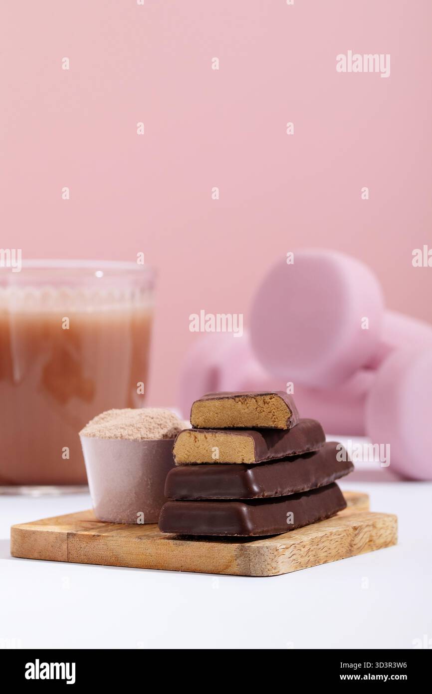 Gros plan d'une boisson protéinée, de barres protéinées et de poudre protéinée sur fond d'équipement d'entraînement rose, capturant l'essence du fitness n Banque D'Images