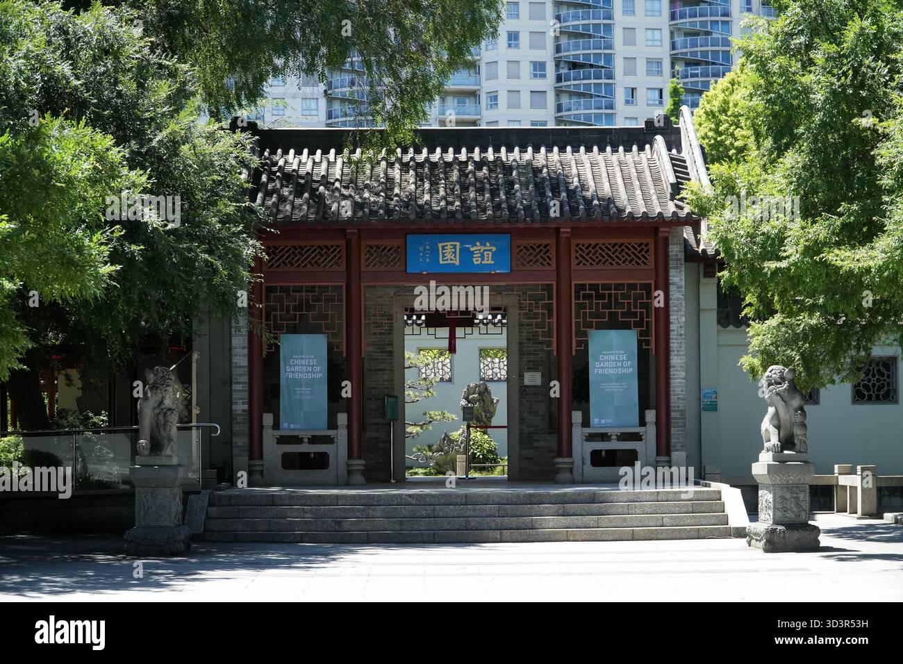 Jardin chinois de l'amitié. Porte d'entrée avec architecture traditionnelle, statues de lion en pierre et bâtiments de ville modernes en arrière-plan, Sydney, au Banque D'Images