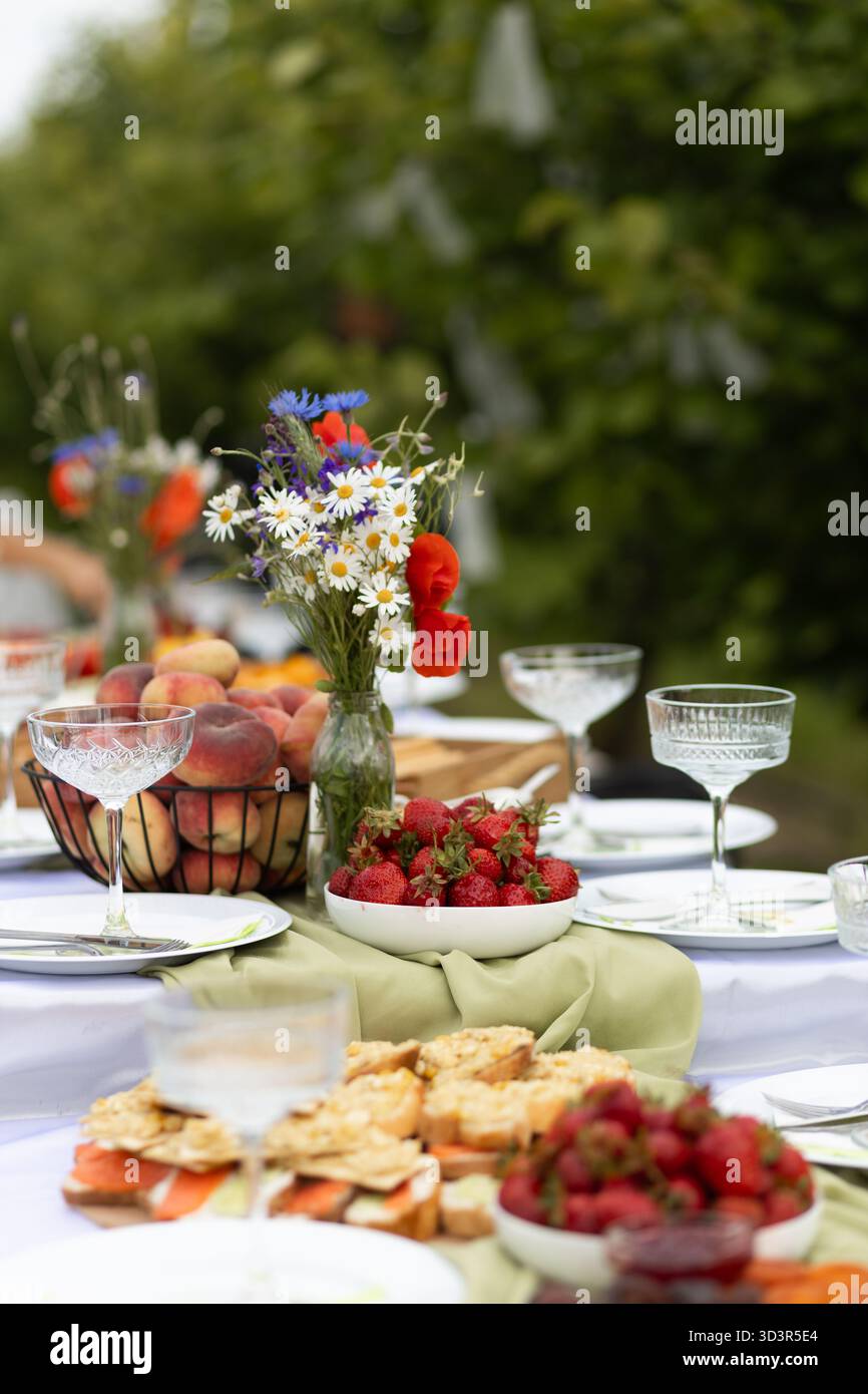 Un cadre de brunch extérieur magnifiquement aménagé avec des fruits d'été vibrants comme des fraises et des pêches, complétés par des compositions florales fraîches Banque D'Images