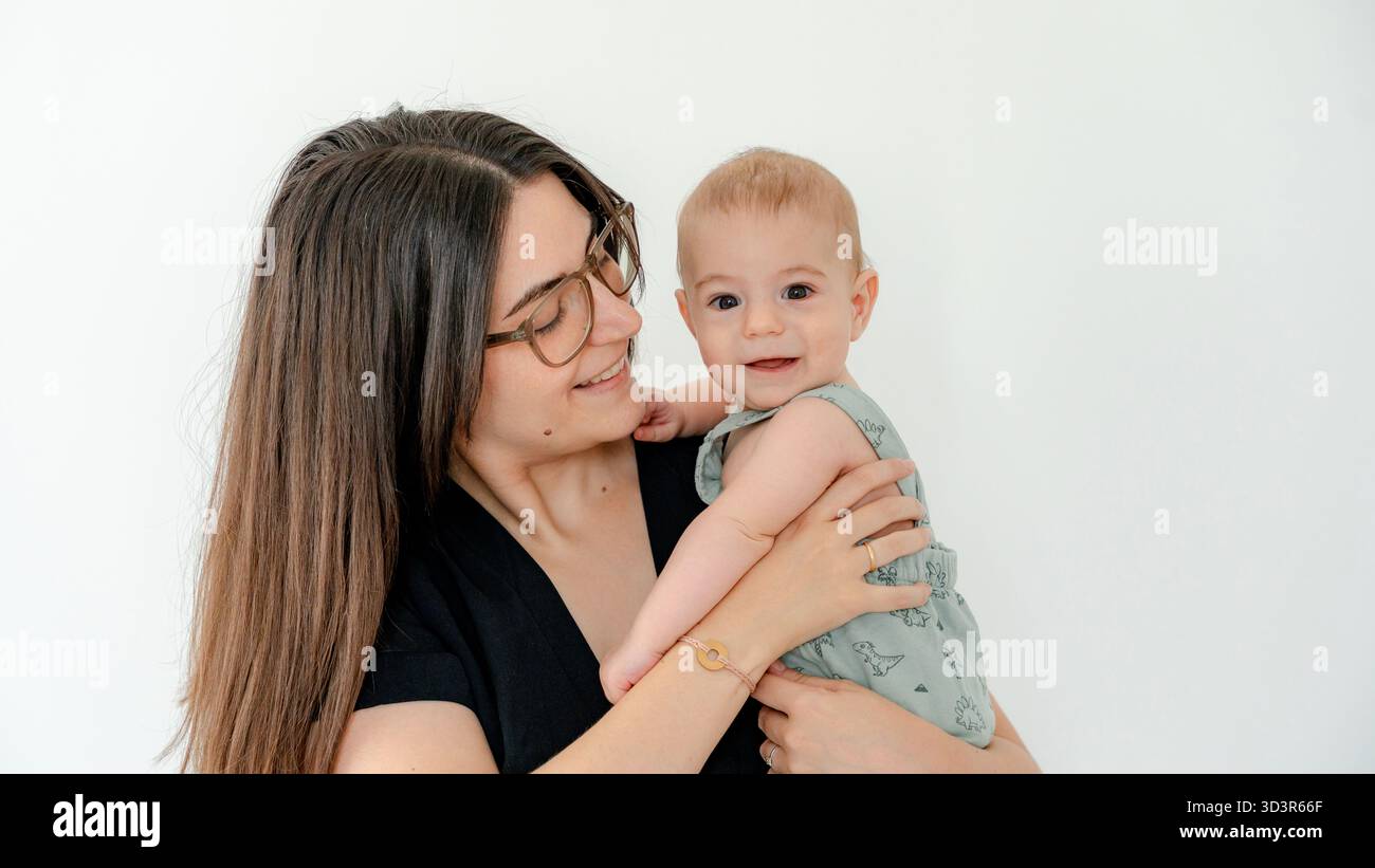 Une mère joyeuse embrasse son bébé heureux dans un câlin chaleureux et aimant, capturant un beau moment de lien familial et de développement de la petite enfance contre Banque D'Images
