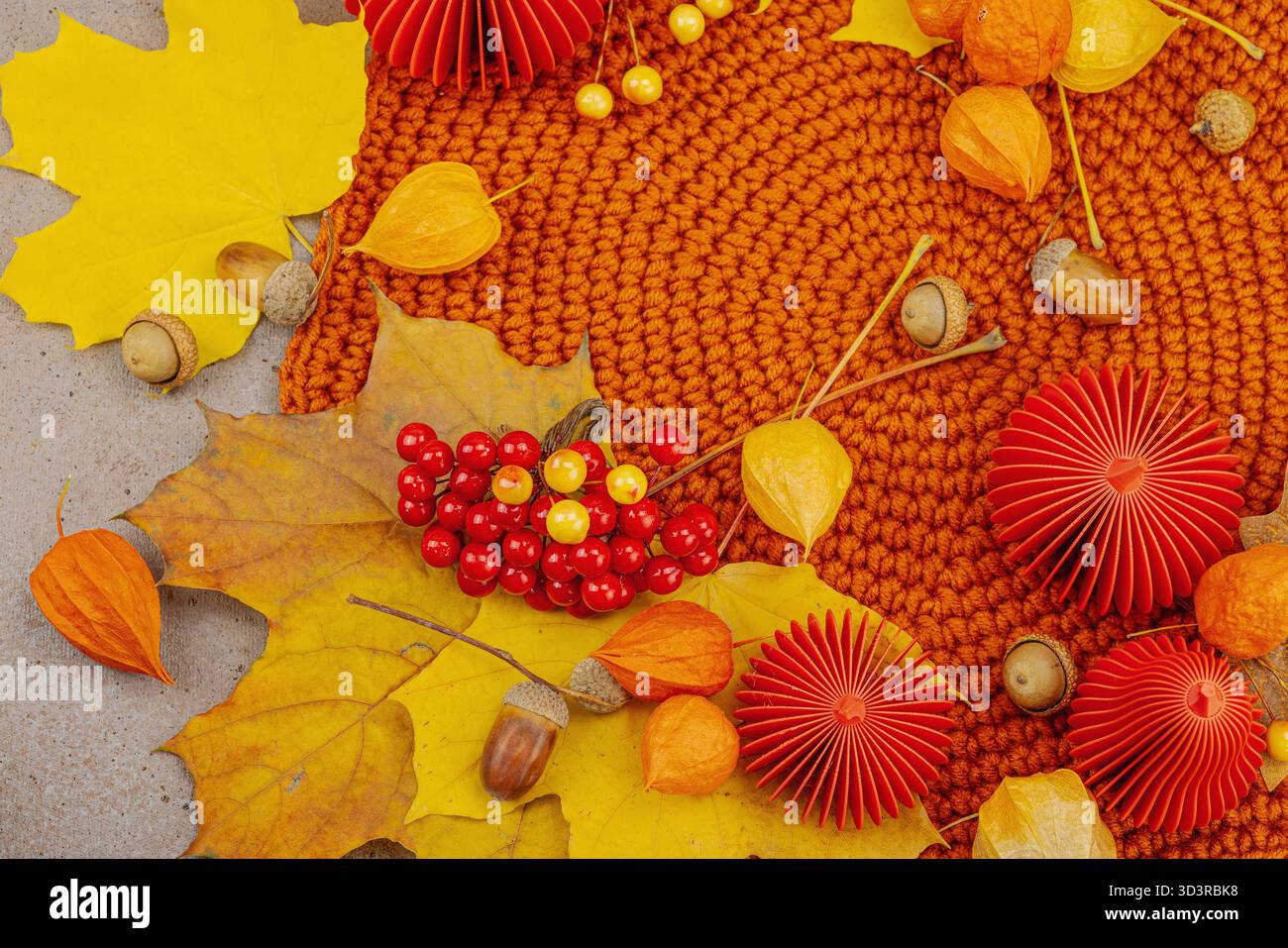 Nature morte d'automne avec citrouilles en papier rouge, glands, feuilles d'érable jaunes et physalis sur un fond texturé. Composition saisonnière confortable, slow living Banque D'Images