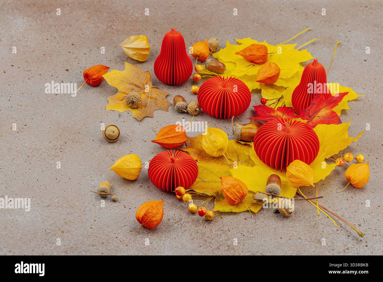 Nature morte d'automne avec citrouilles en papier rouge, glands, feuilles d'érable jaunes et physalis sur un fond texturé. Composition saisonnière confortable, slow living Banque D'Images