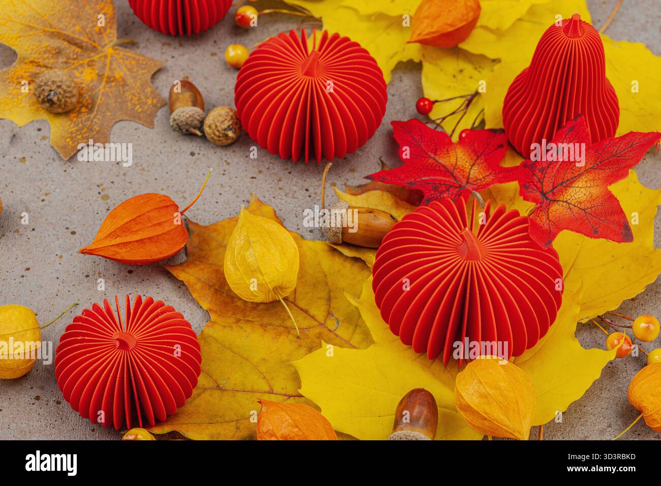 Nature morte d'automne avec citrouilles en papier rouge, glands, feuilles d'érable jaunes et physalis sur un fond texturé. Composition saisonnière confortable, slow living Banque D'Images